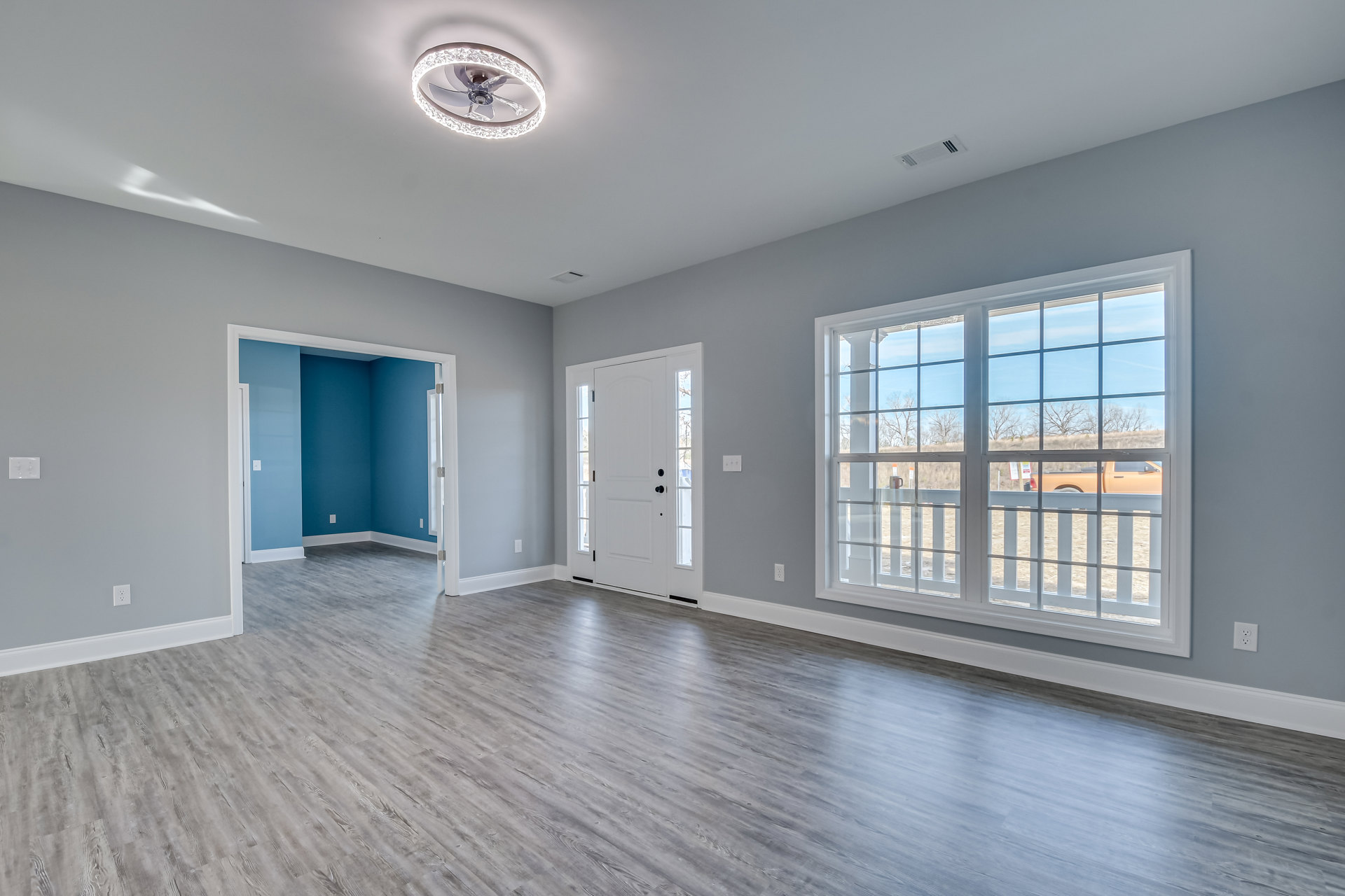 Wood floor room with white walls, ceiling fan featuring light ring, white-framed window, and white door with black hardware
