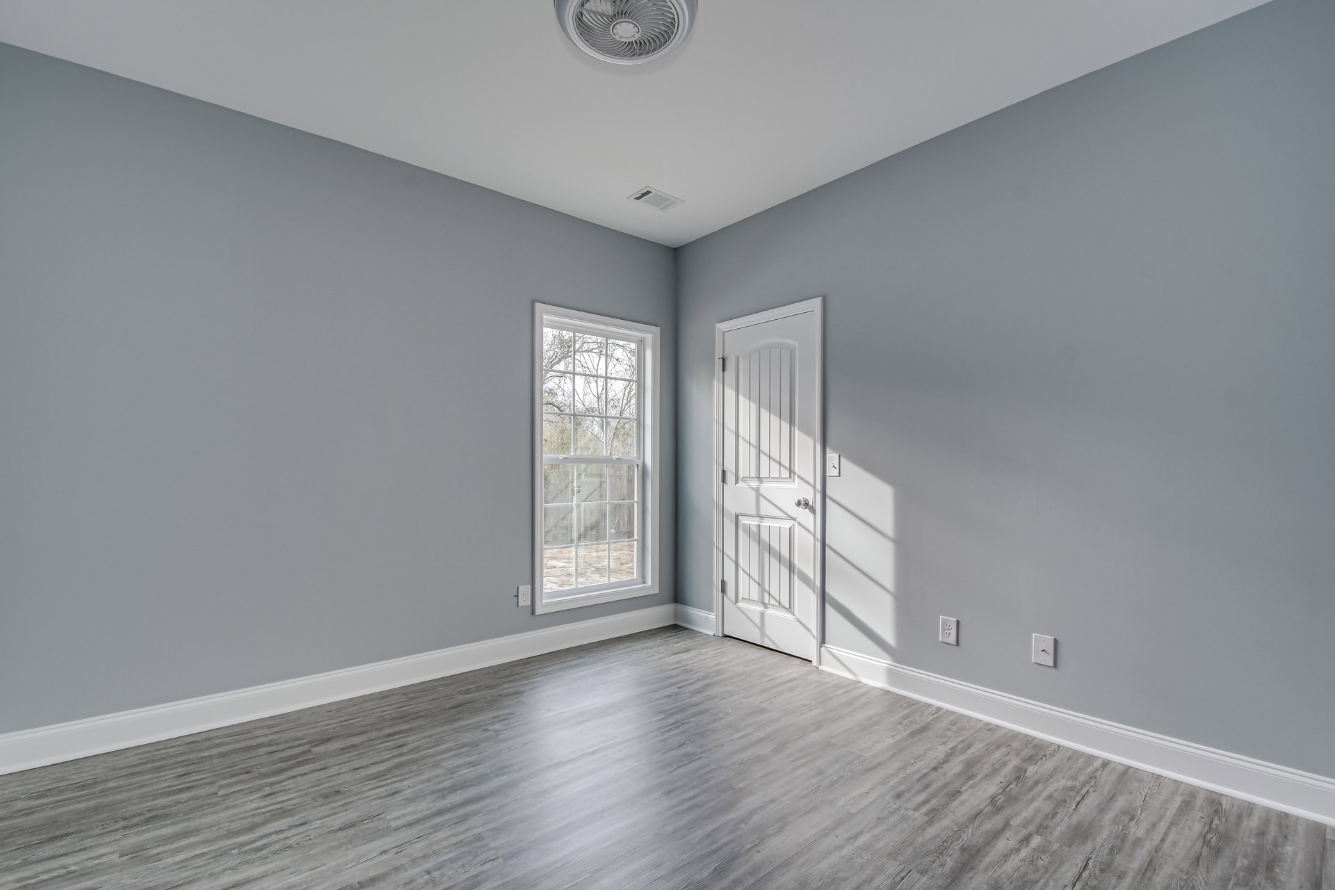 White paneled door with glass inserts, wood laminate flooring, large window overlooking green trees, ceiling fan, light-colored plaster walls with crown molding