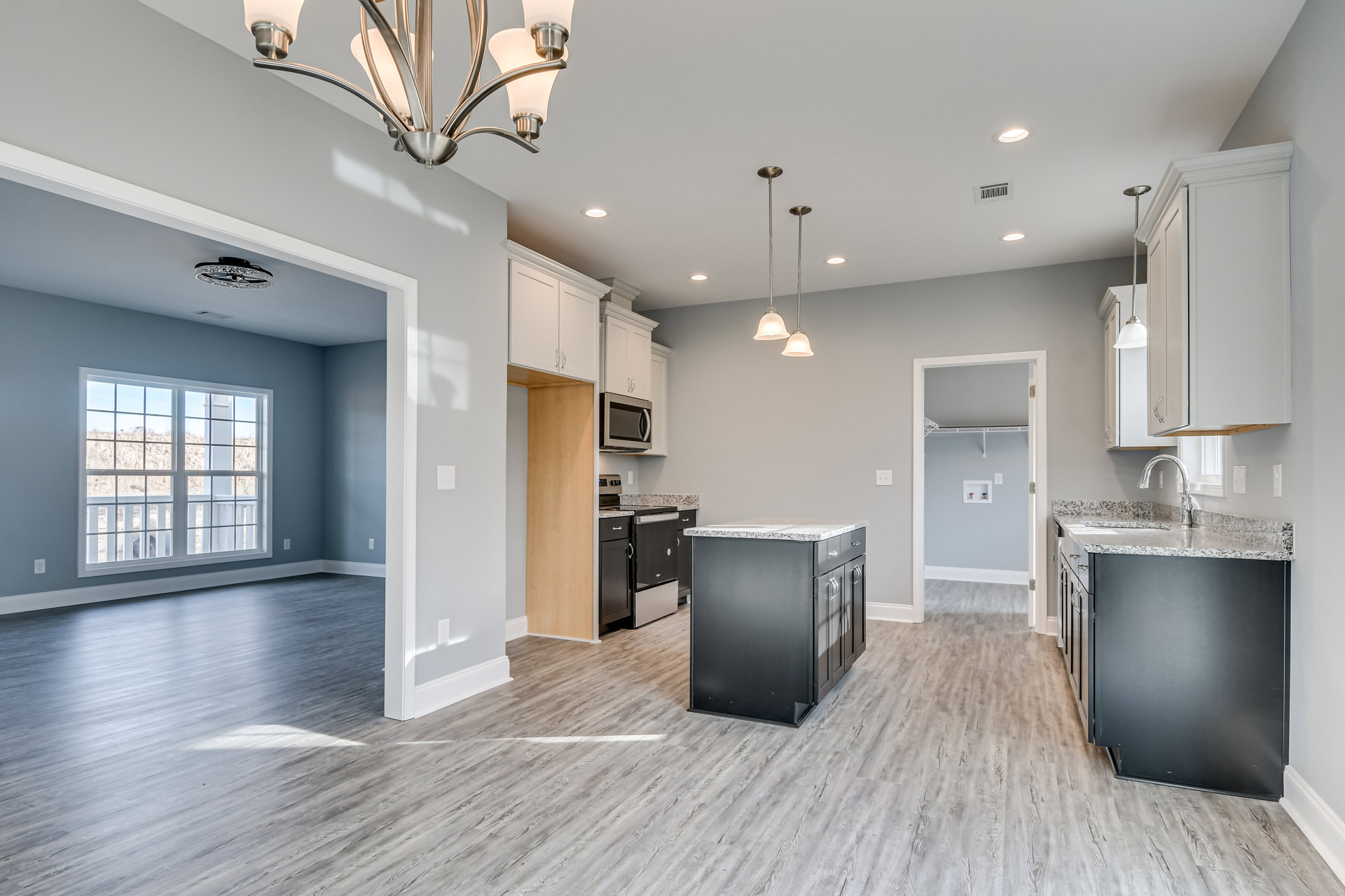 Open kitchen and dining area featuring wood flooring, marble-topped island, built-in microwave, chandelier, window overlooking a field, and kitchen counter with sink.