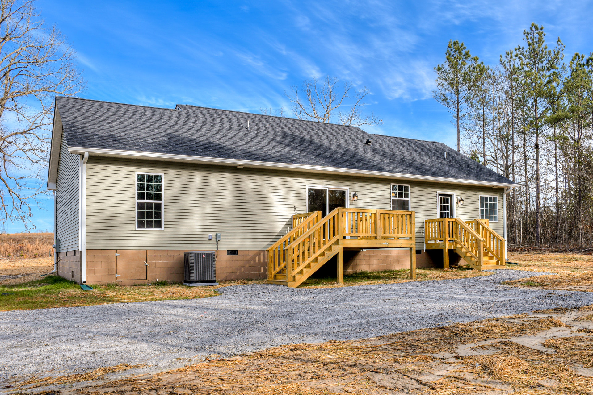 Wooden staircase with metal railing leads to front entrance of modern cottage-style home, large multi-pane window, concrete base, black square heater, surrounded by trees and