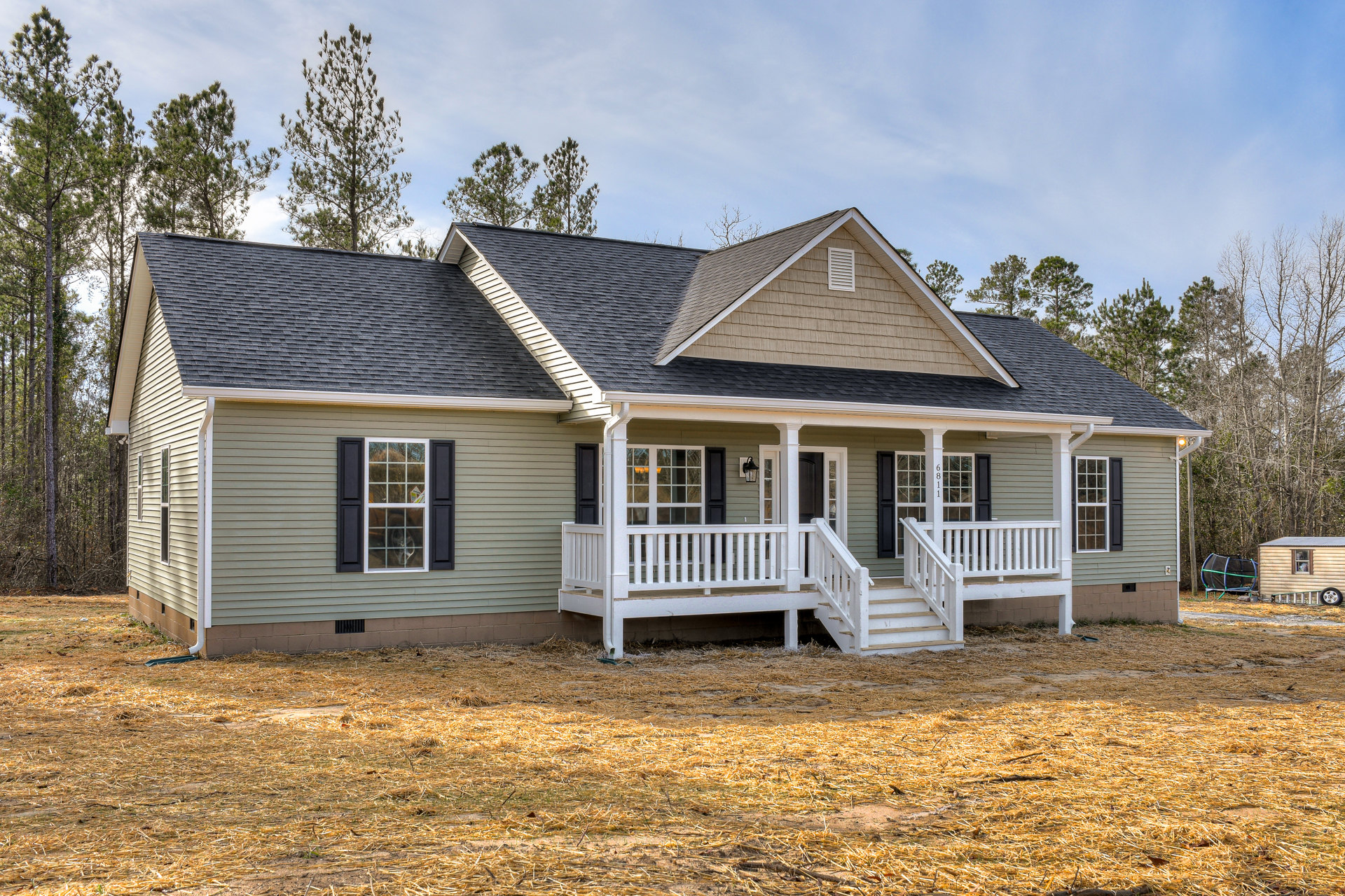 Two-story house with light siding, white porch railing, front yard with green grass, trampoline, white bench, and a dog visible through a window