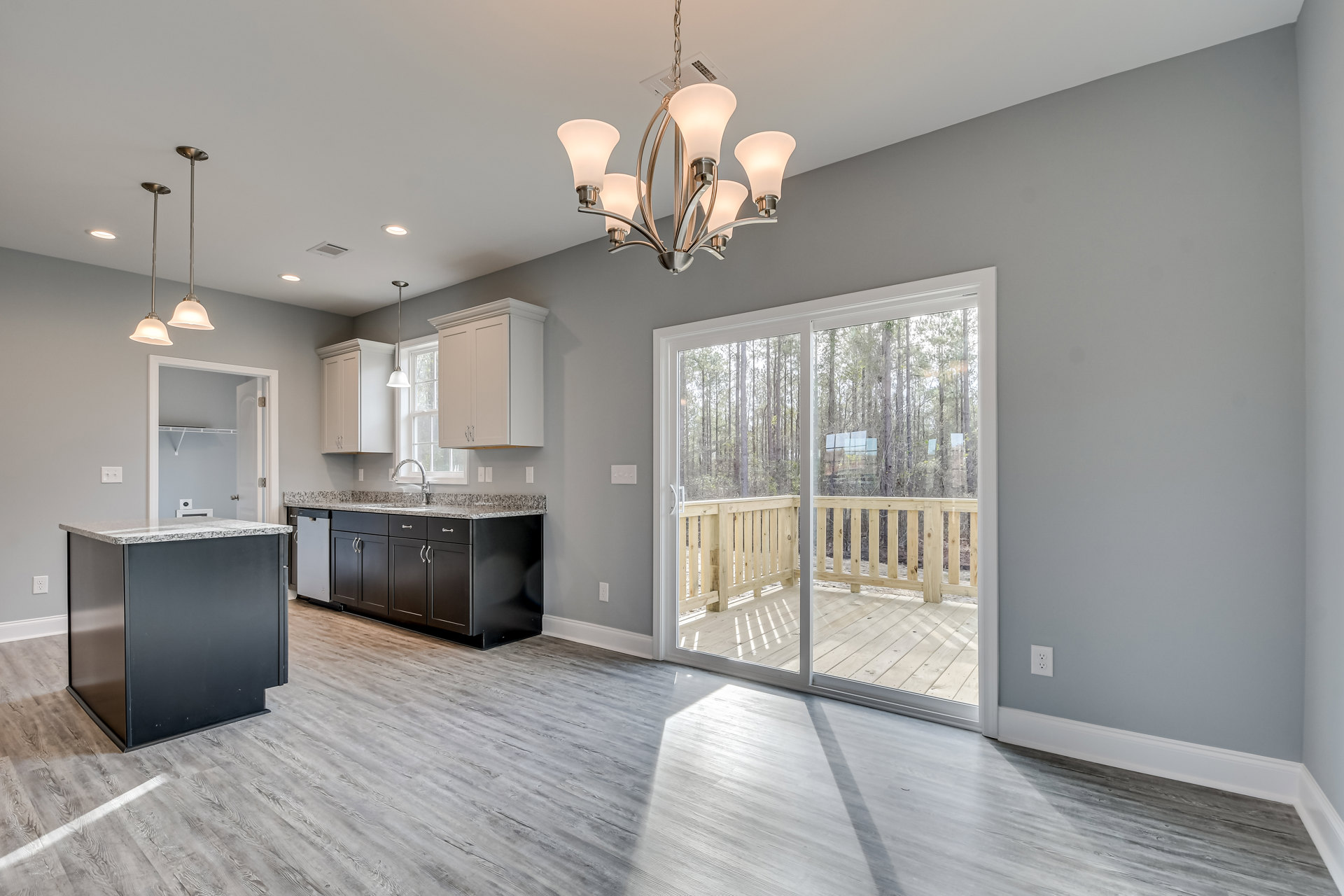 Modern kitchen featuring a black and white island, granite countertops, cabinetry, five-light ceiling fixture, white laminate flooring, and a glass door opening to a deck.