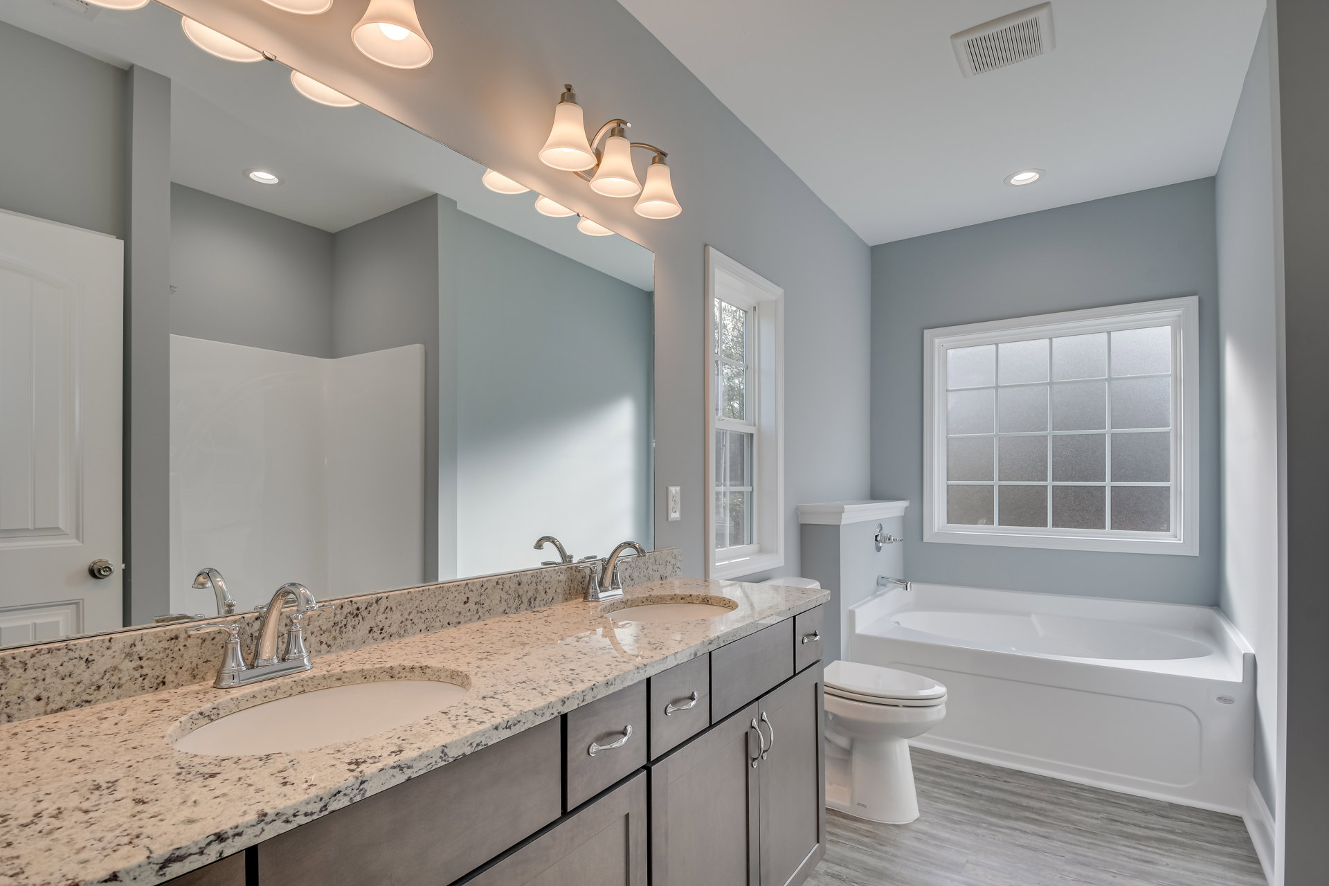 Bathroom with freestanding tub, white sink and faucet on stone countertop, frosted glass window, closed toilet, light tile flooring, and neutral cabinetry