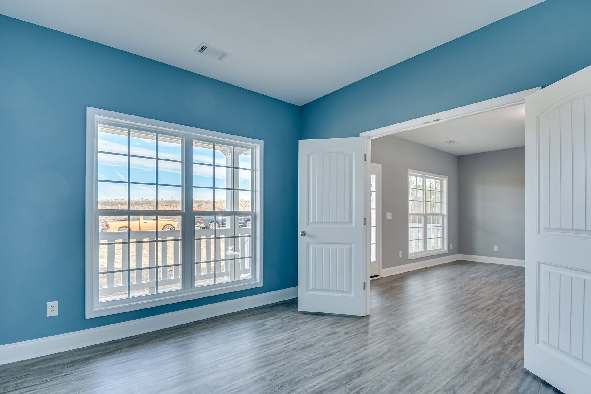 White paneled door open in a room with multi-pane window, laminate flooring, plaster walls, and decorative molding.