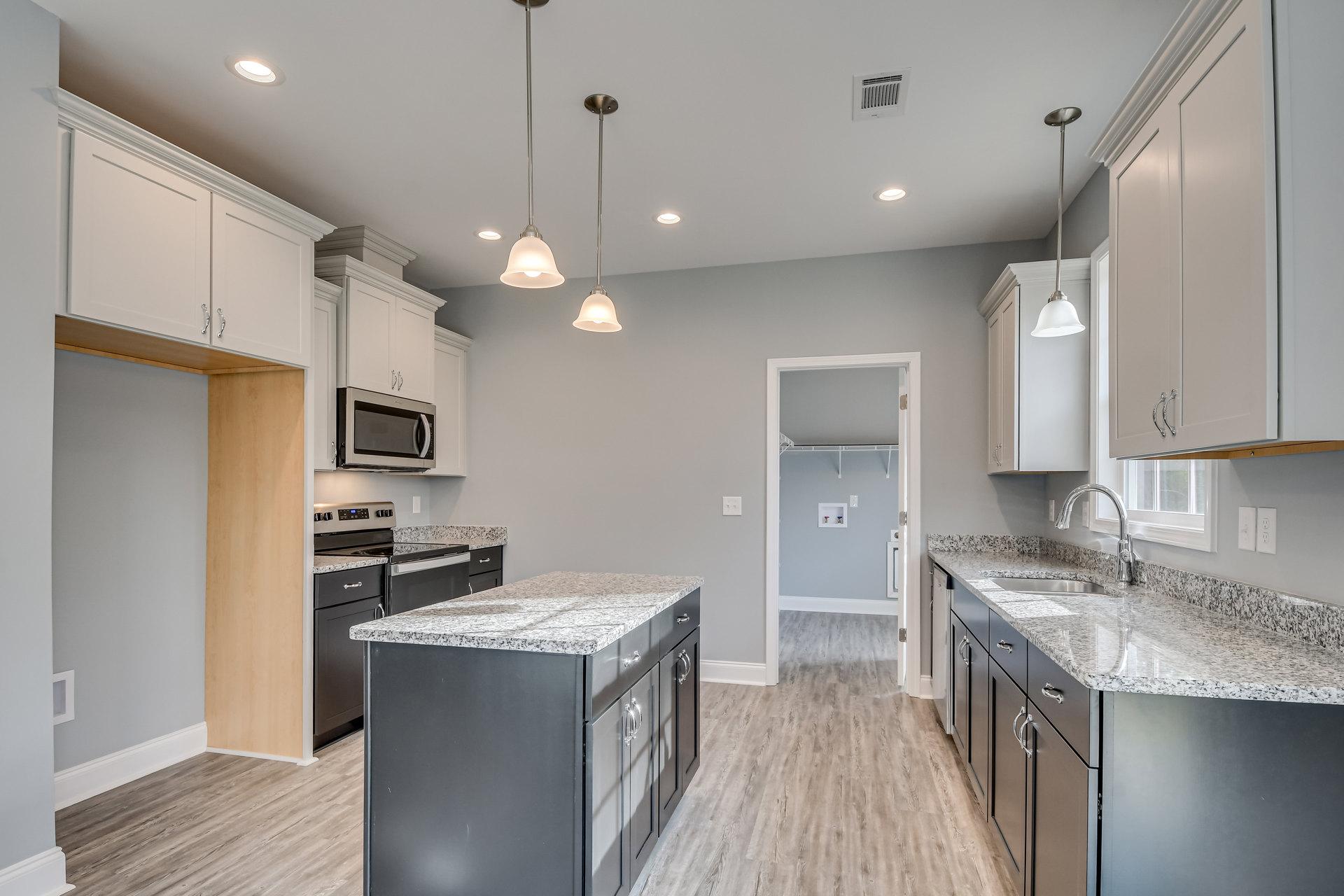 Kitchen with granite countertops, wood flooring, white cabinetry, built-in microwave, kitchen island, ceiling vent, metal light fixture, and sink.
