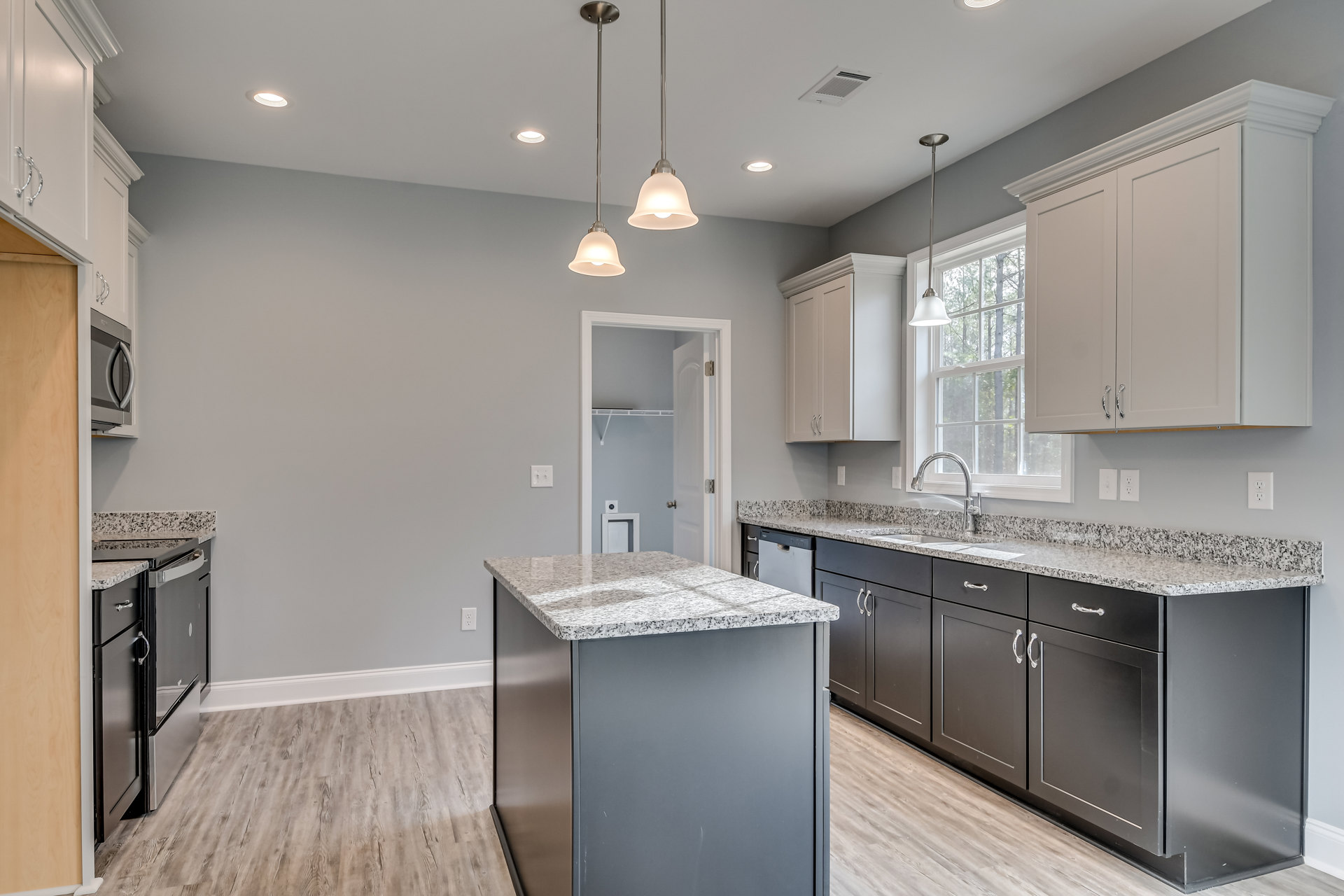 Marble island with waterfall edge, white cabinetry, stainless steel sink and faucet, tile backsplash, built-in appliances, recessed lighting, and light wood flooring