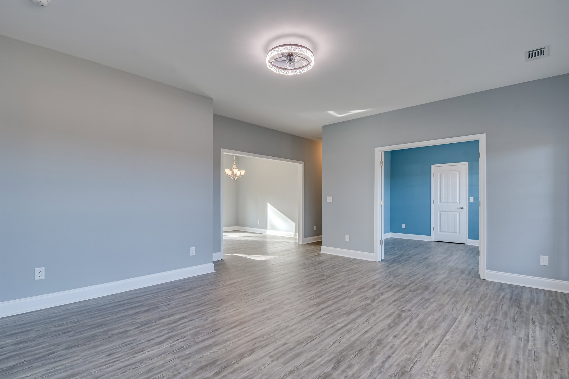 Wood floor room with white walls, ceiling fan featuring a light ring, white door with silver handle, and decorative molding along the ceiling.