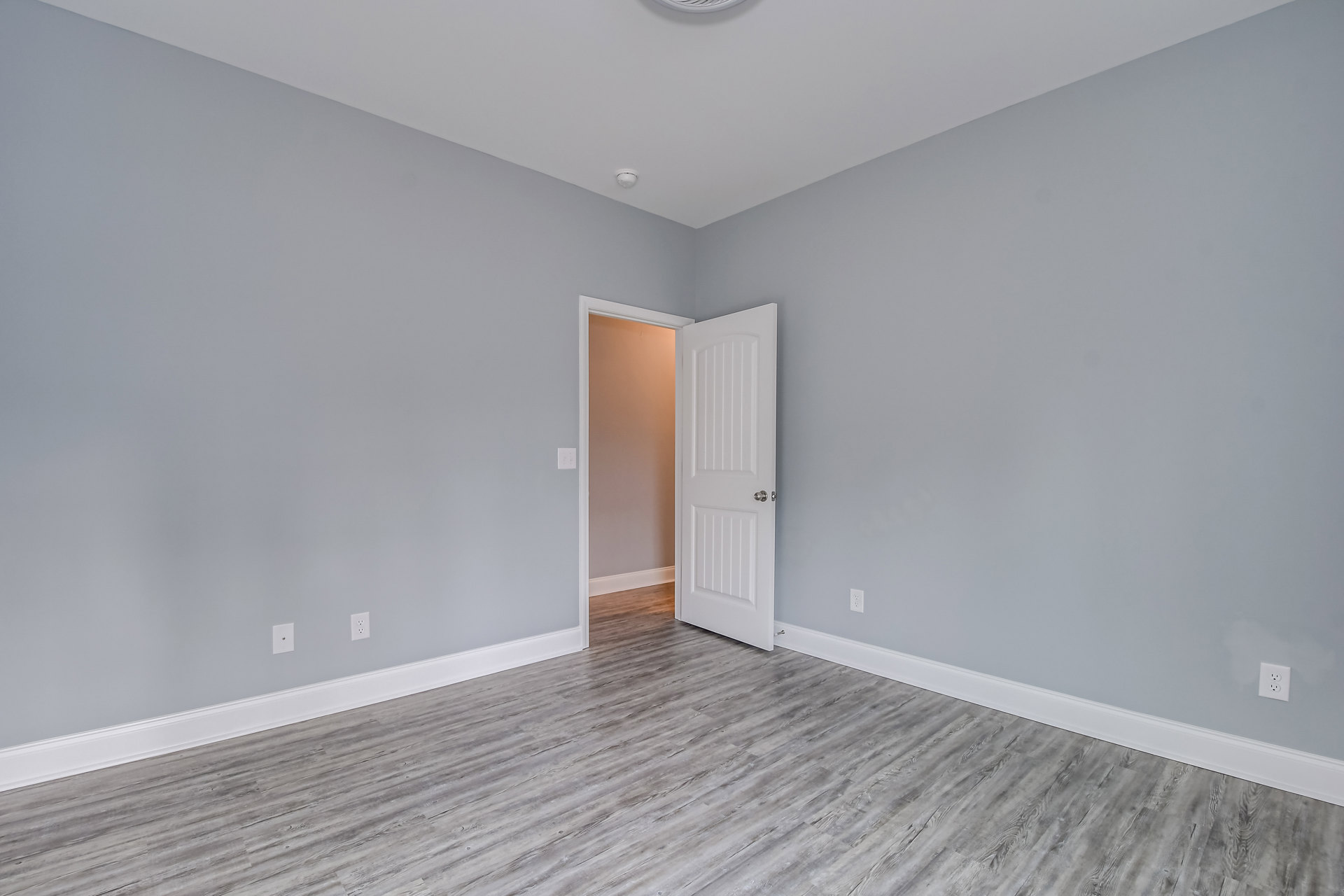 White paneled door with silver knob open to reveal bright light, laminate flooring, plaster walls, ceiling molding, and smoke detector visible.