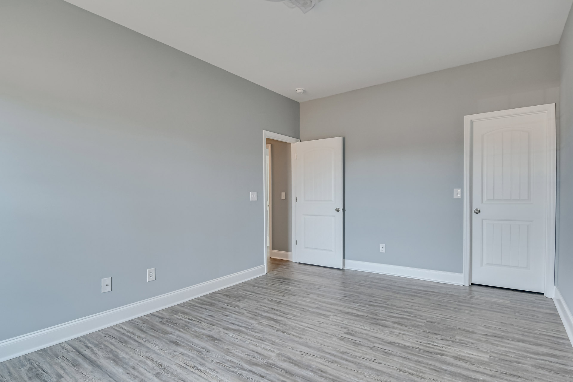 White paneled door with silver knob open onto wood laminate flooring, white walls, and ceiling with smoke detector and crown molding