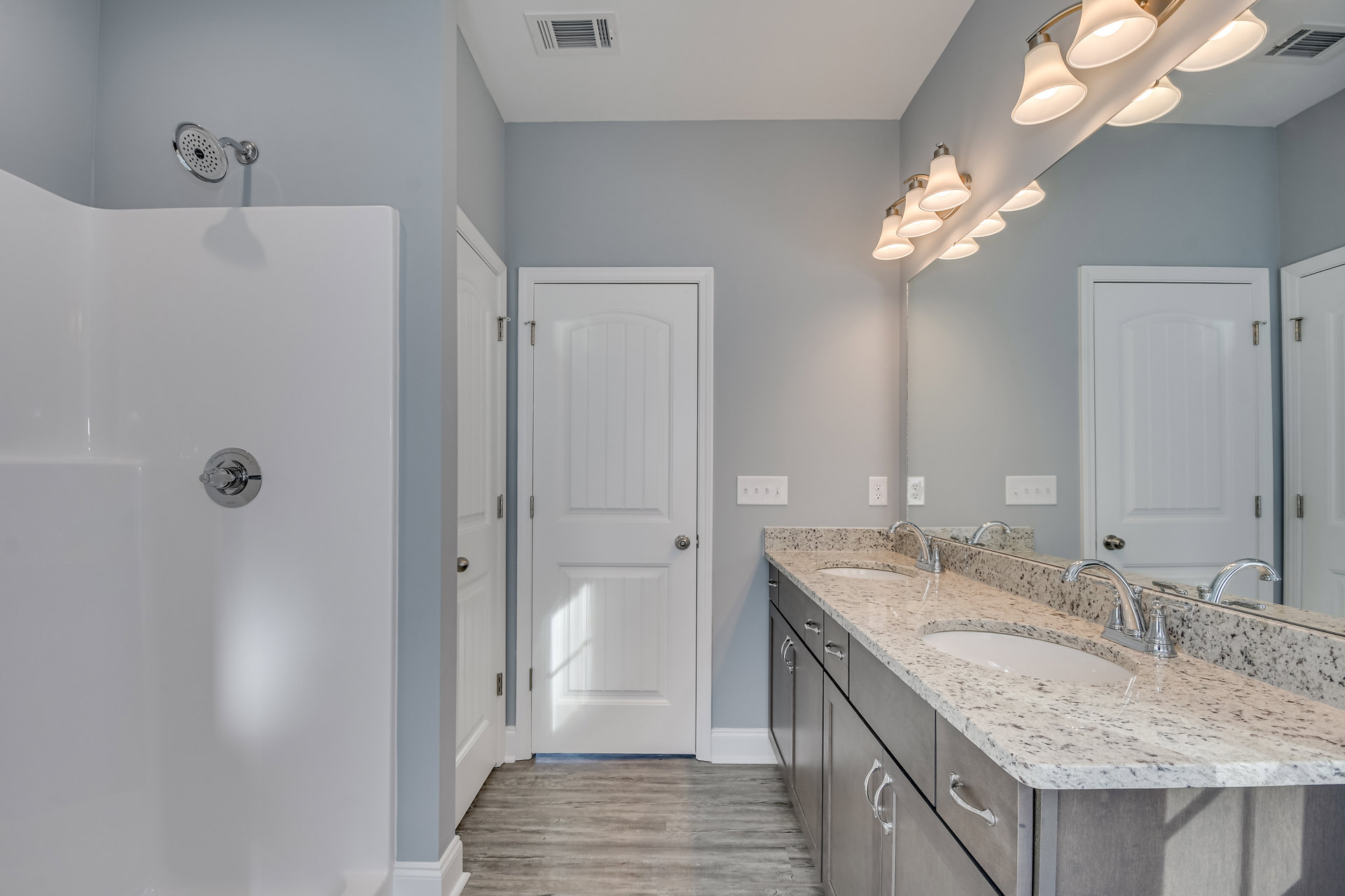 Bathroom with dual sinks set in marble countertops, chrome faucets, white cabinetry, and a white door with silver hardware.