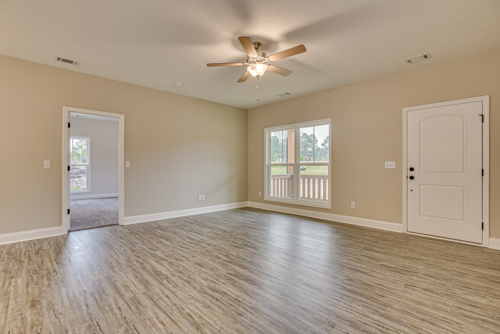 Ceiling fan with light fixture, wood flooring, white door with rope handle, large windows showing outdoor view, plaster walls