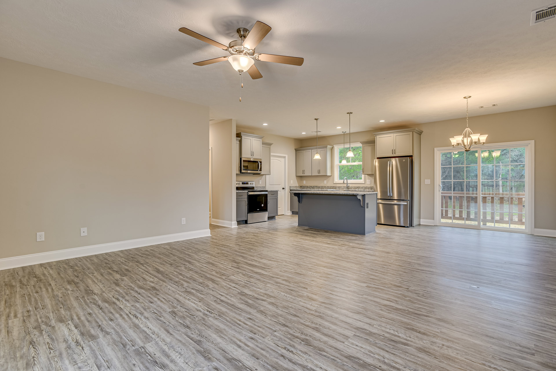 Open-concept kitchen and living room with wood flooring, stainless steel refrigerator, ceiling fan with light fixture, built-in microwave, glass door, chandelier, and fireplace.