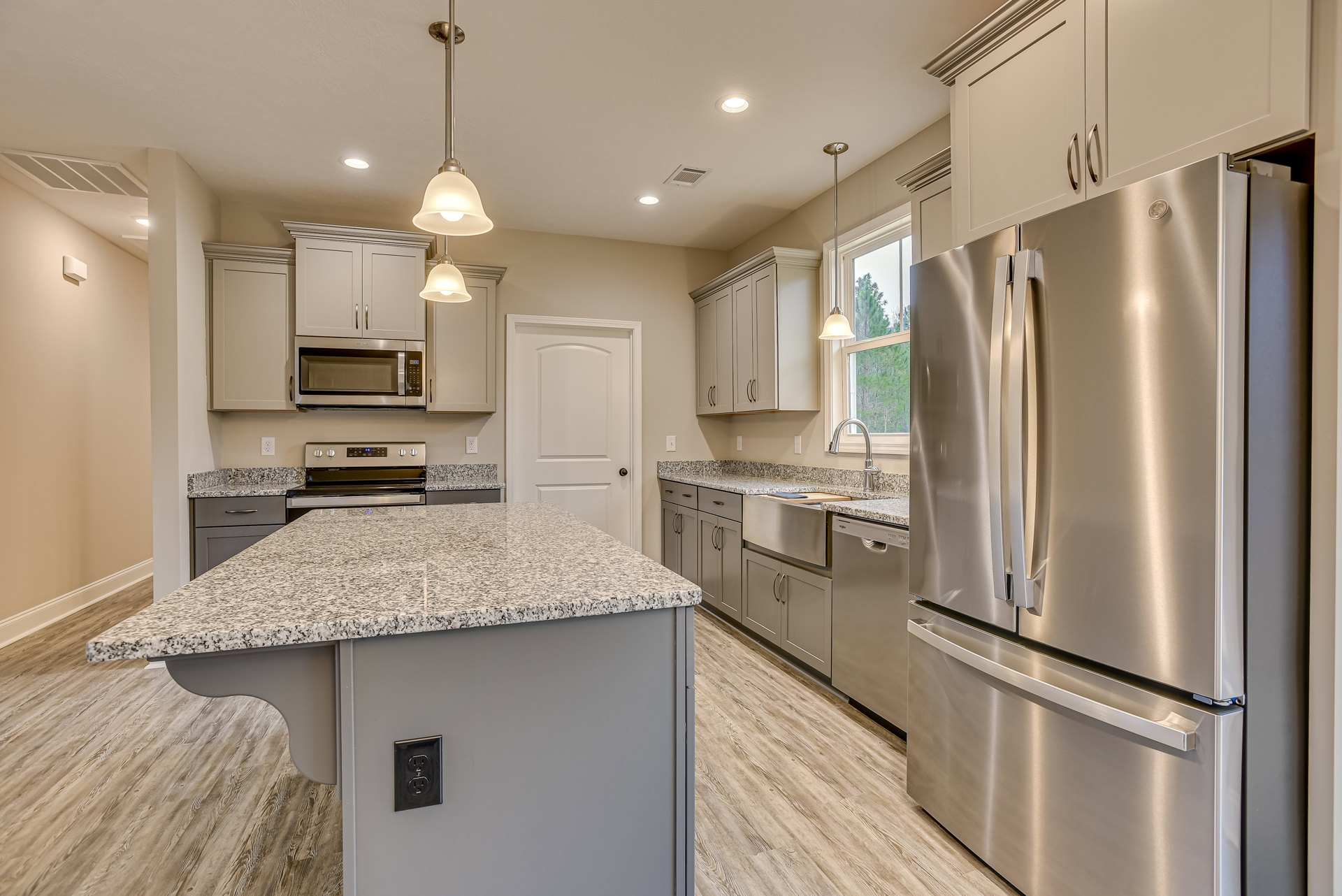 Kitchen with marble-topped island, stainless steel refrigerator, built-in microwave, white cabinetry, and modern outlet on backsplash