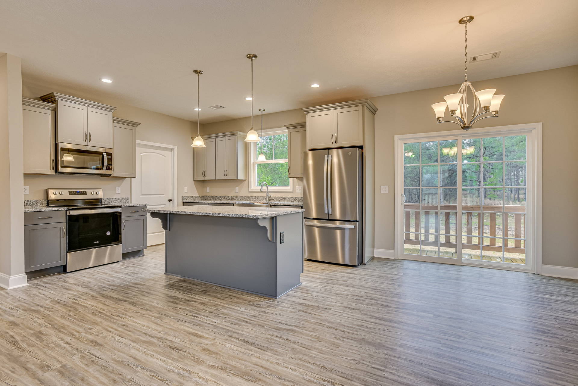 Spacious kitchen featuring a large central island with stone countertop, stainless steel refrigerator, built-in stove and oven, white microwave, wood cabinetry, and sliding glass