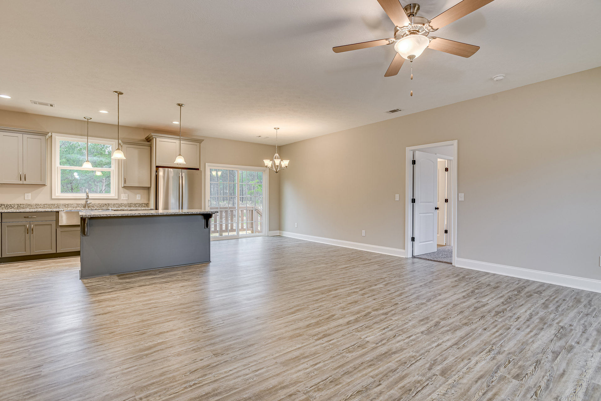 Open floor plan featuring hardwood floors, central kitchen island with white cabinetry, ceiling fan with light fixture, two white doors with black handles, glass door offering