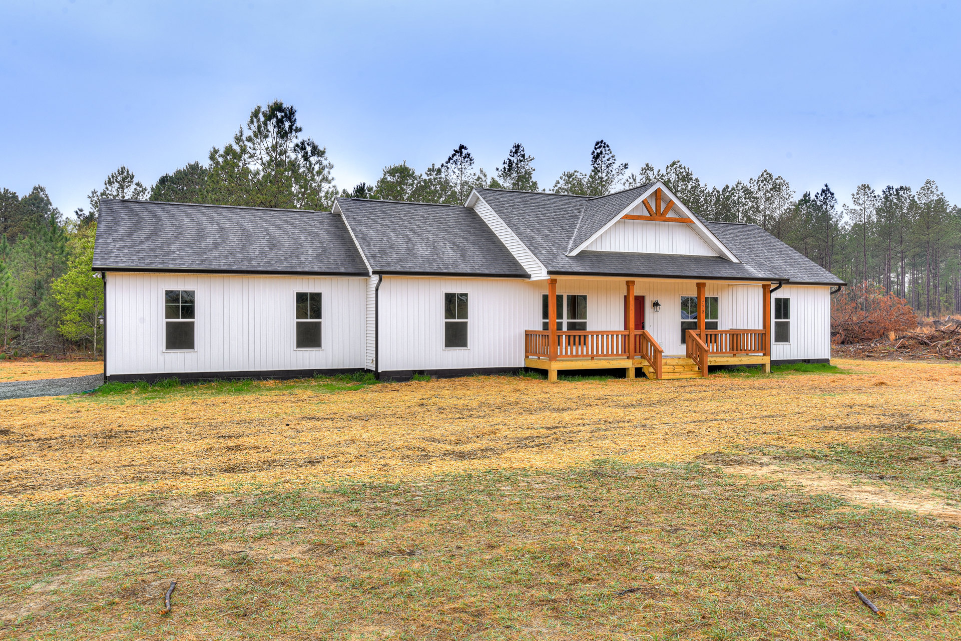 White farmhouse with wooden porch and railing, expansive grassy yard, mature trees, and large windows.