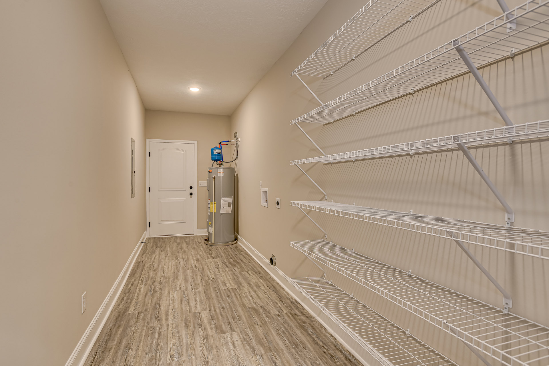 Hallway with white plaster walls, white metal shelving, composite flooring, white door with black handle, water cooler, and refrigerator