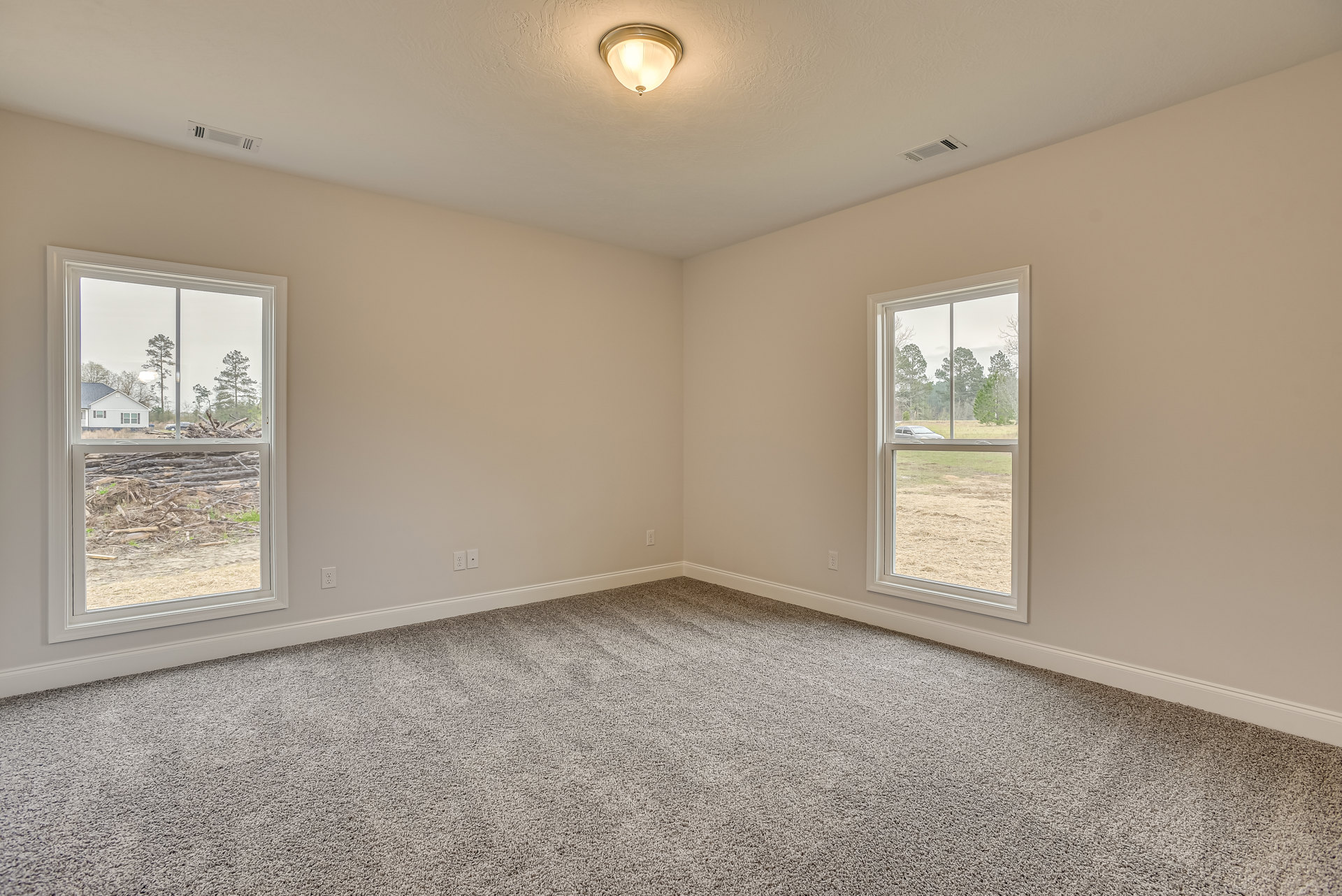Carpeted room with white walls, multiple windows, ceiling light fixture, and a view of a car and stacked wood outside.