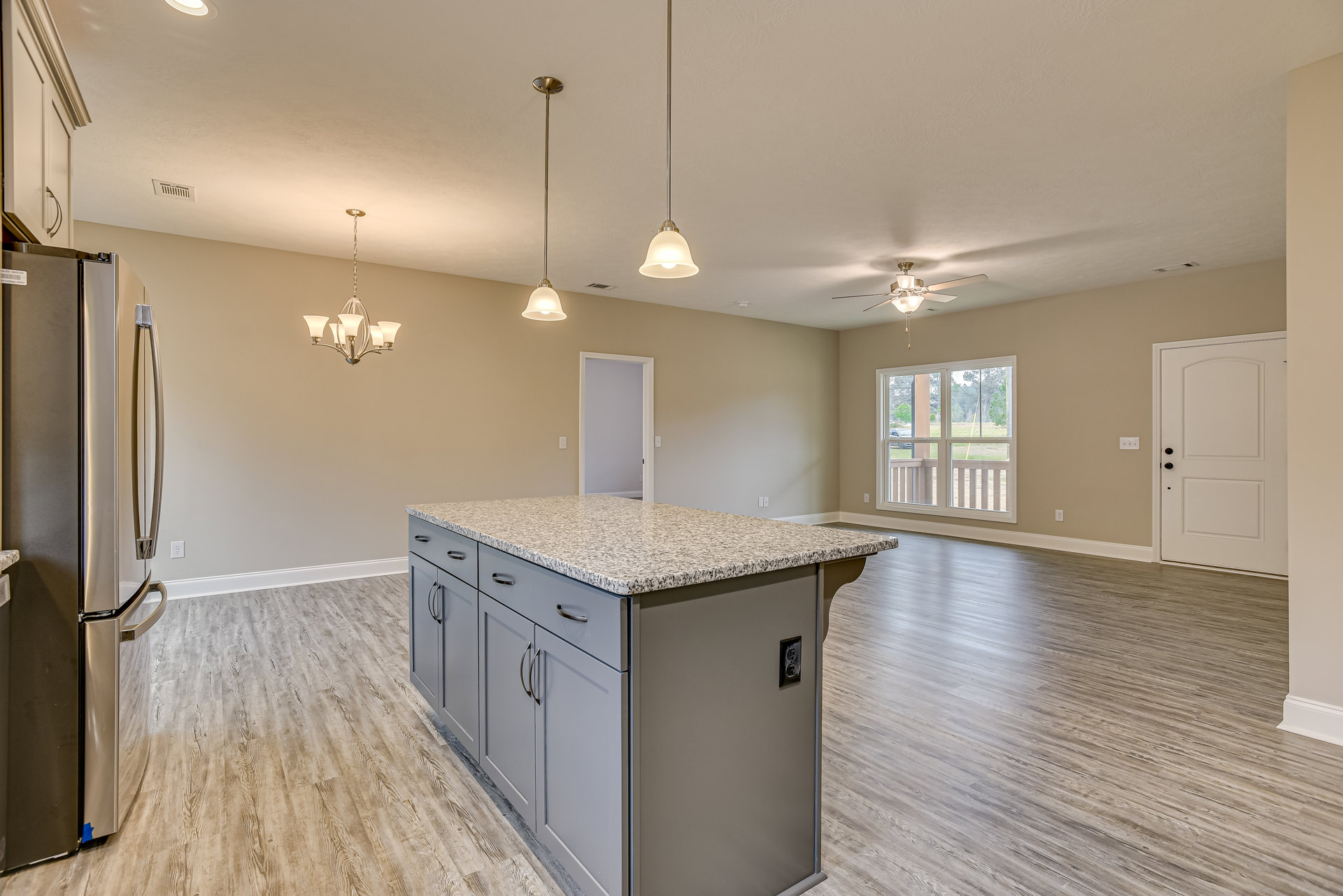 Granite kitchen island with built-in sink, stainless steel refrigerator, tile flooring, white cabinetry, pendant lighting, window overlooking yard and trees, white door with black