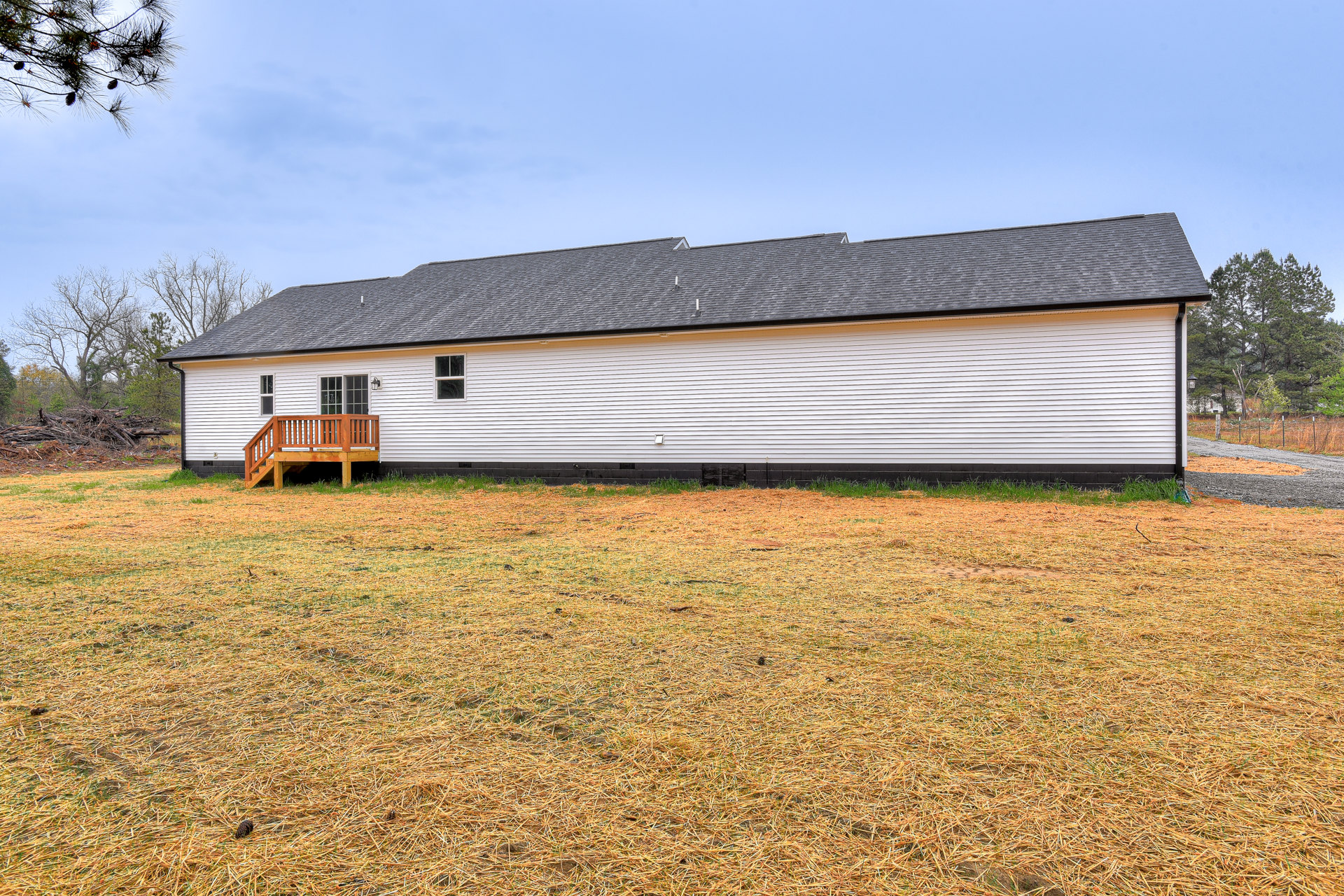 White modern house with horizontal siding, expansive wooden deck with railing, surrounded by green grass and mature trees, under a cloudy sky.