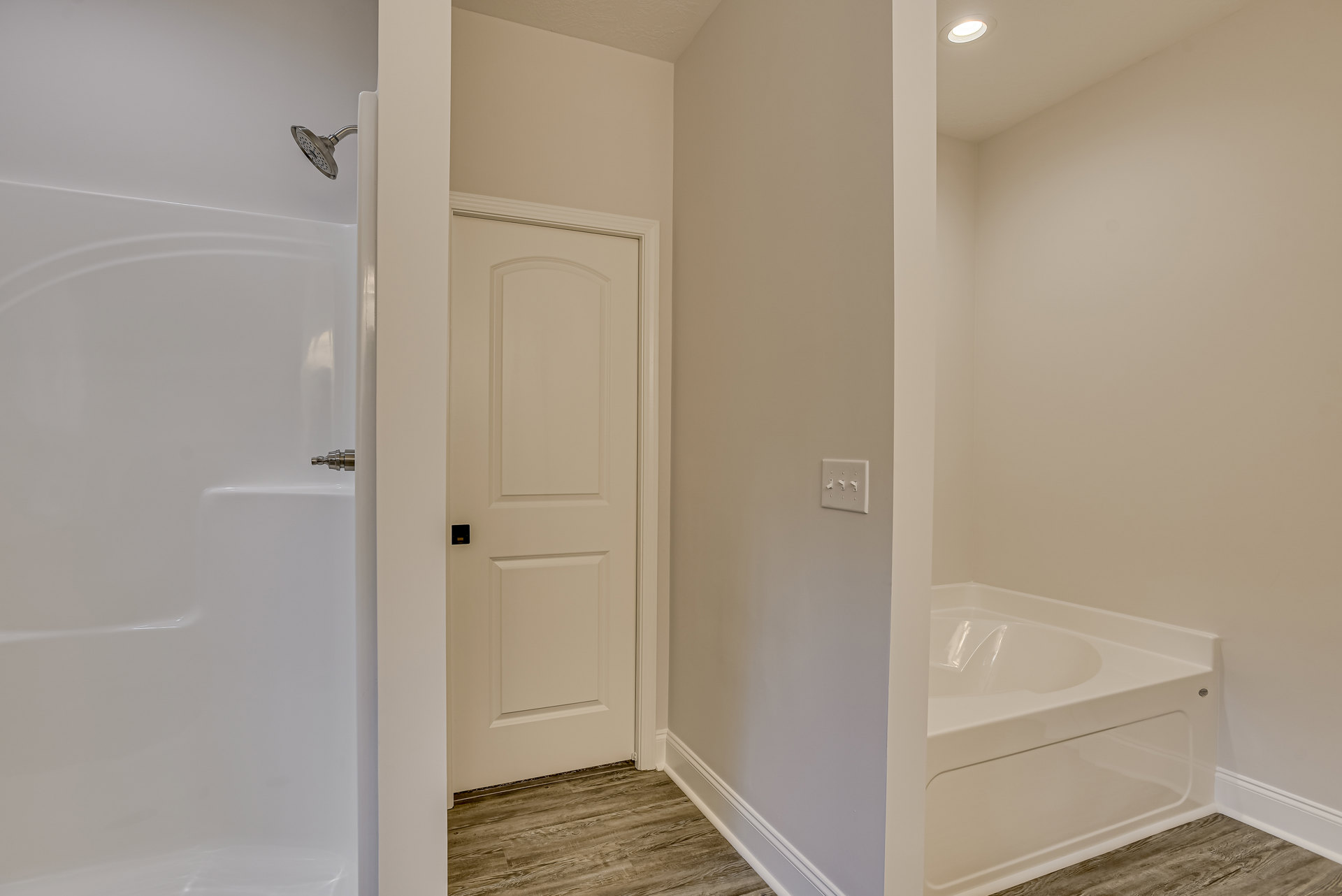 White bathtub with silver faucet set against tiled wall, adjacent to white door with lock and light switch, bathroom floor and plumbing fixtures visible