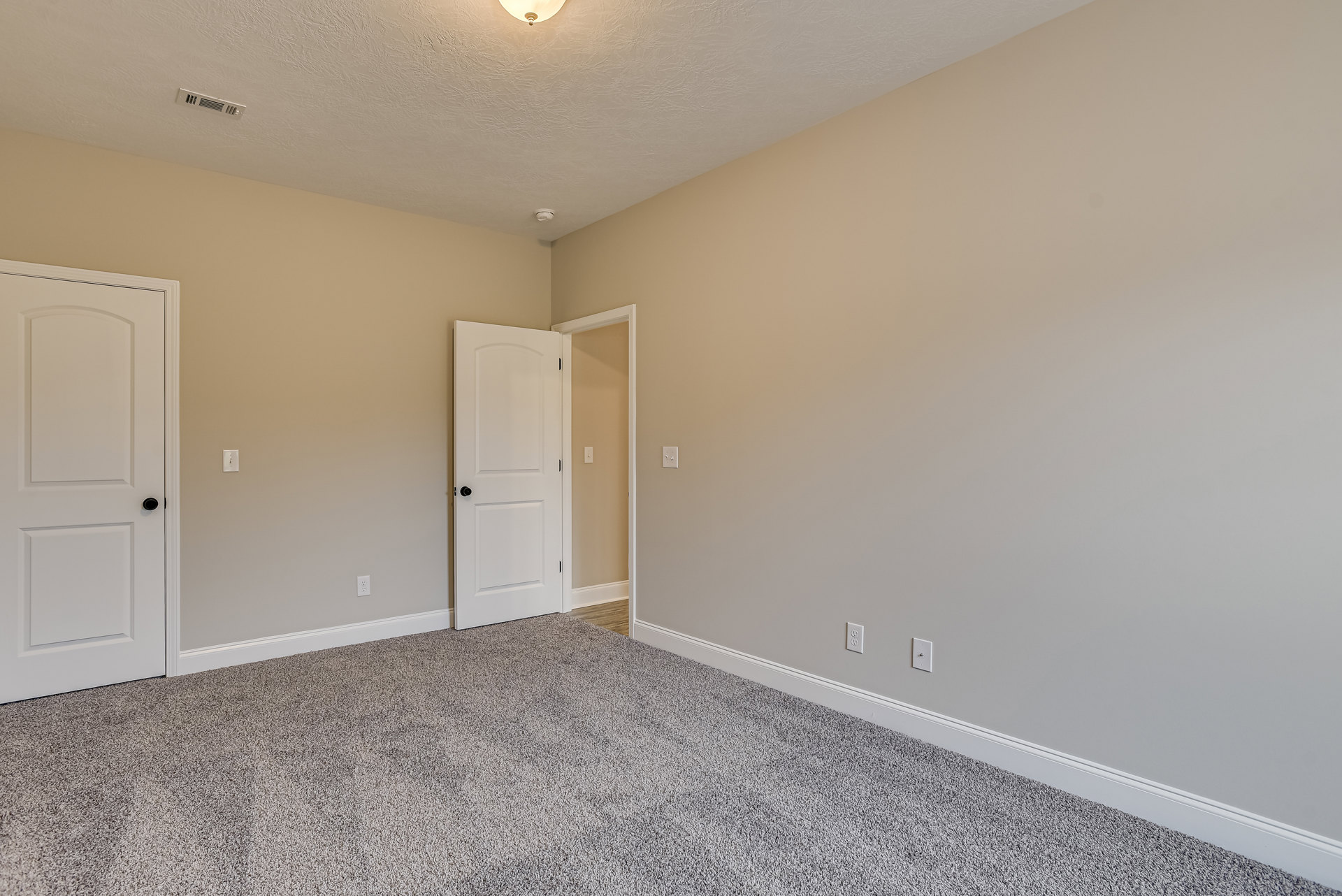 White paneled door with black knob open to carpeted room, light switch on pale wall, smooth plaster ceiling.