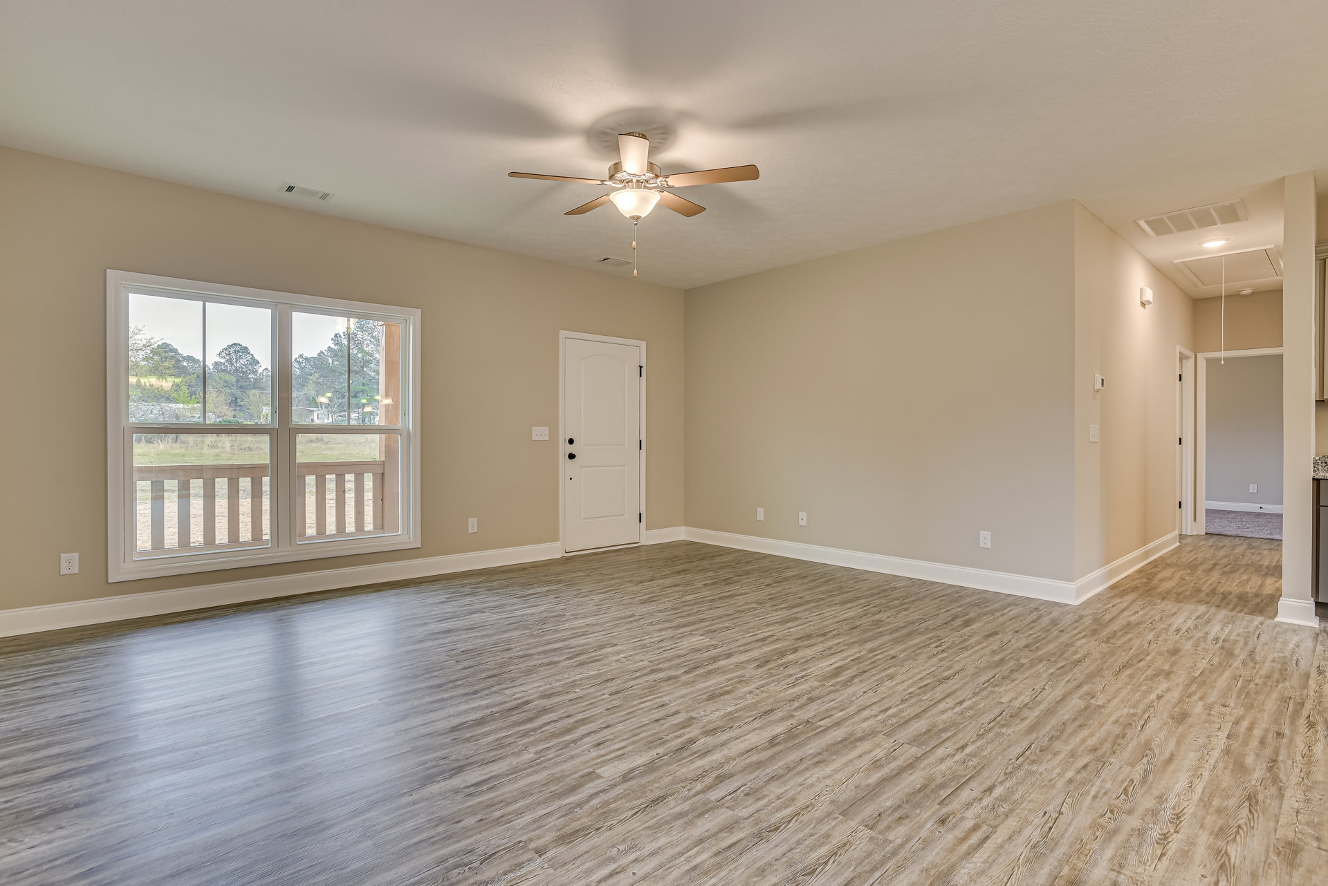 Ceiling fan with light fixture, wood flooring, white door with black knobs, window overlooking field and trees, white walls with molding