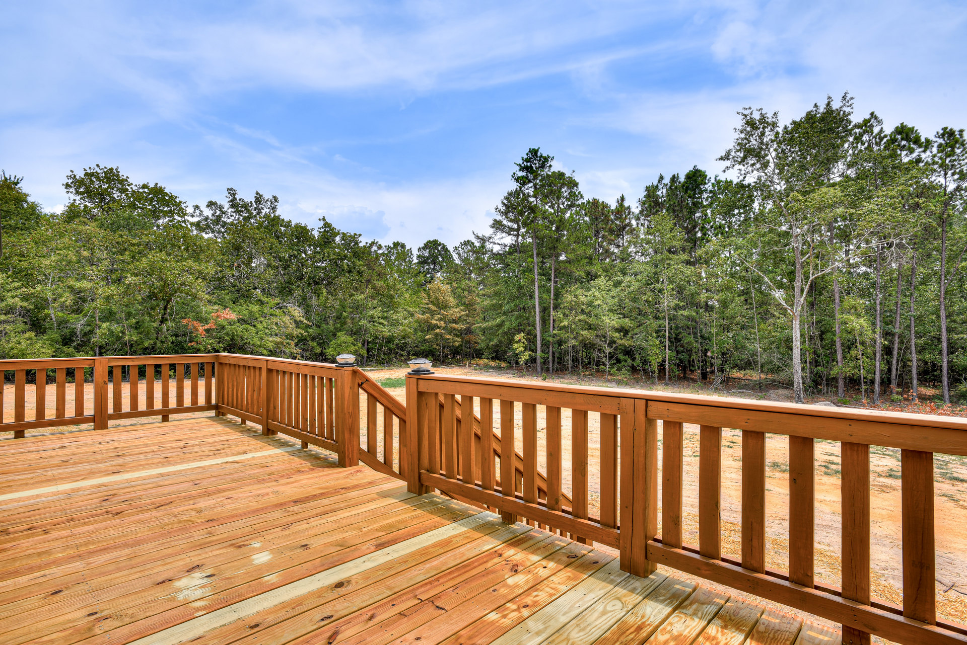 Wood deck with stained planks, wood railing, built-in lights, surrounded by tall trees and greenery in the background