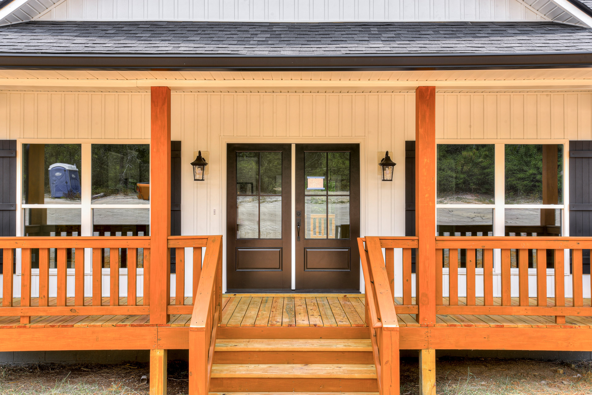 Front porch with wooden steps, double glass-paneled doors, white trim, close-up light fixture, and blue and white portable toilet visible to the side.