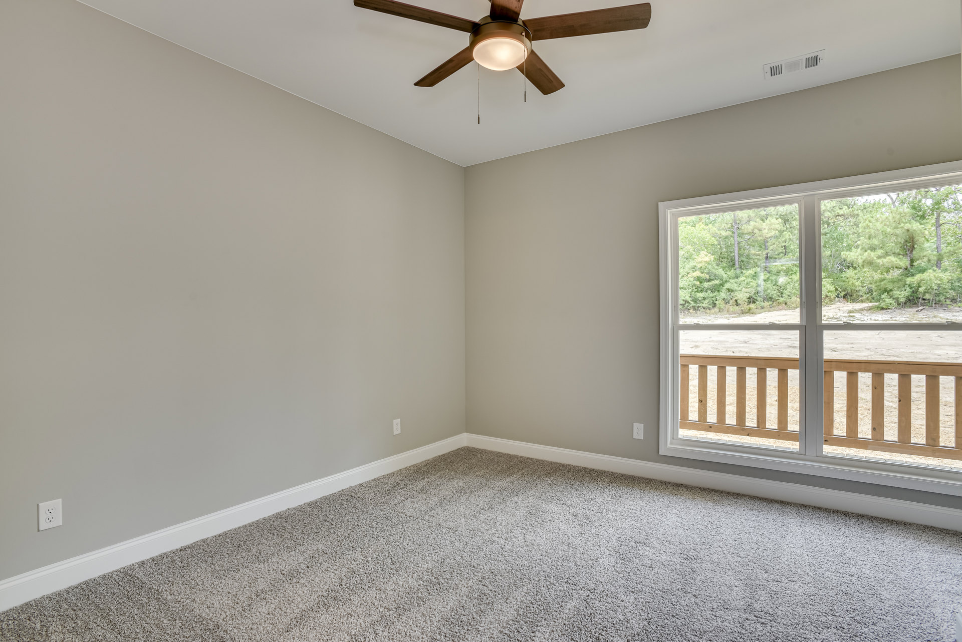 Carpeted room with white walls, ceiling fan with light fixture, large window framed by molding, view of green trees outside