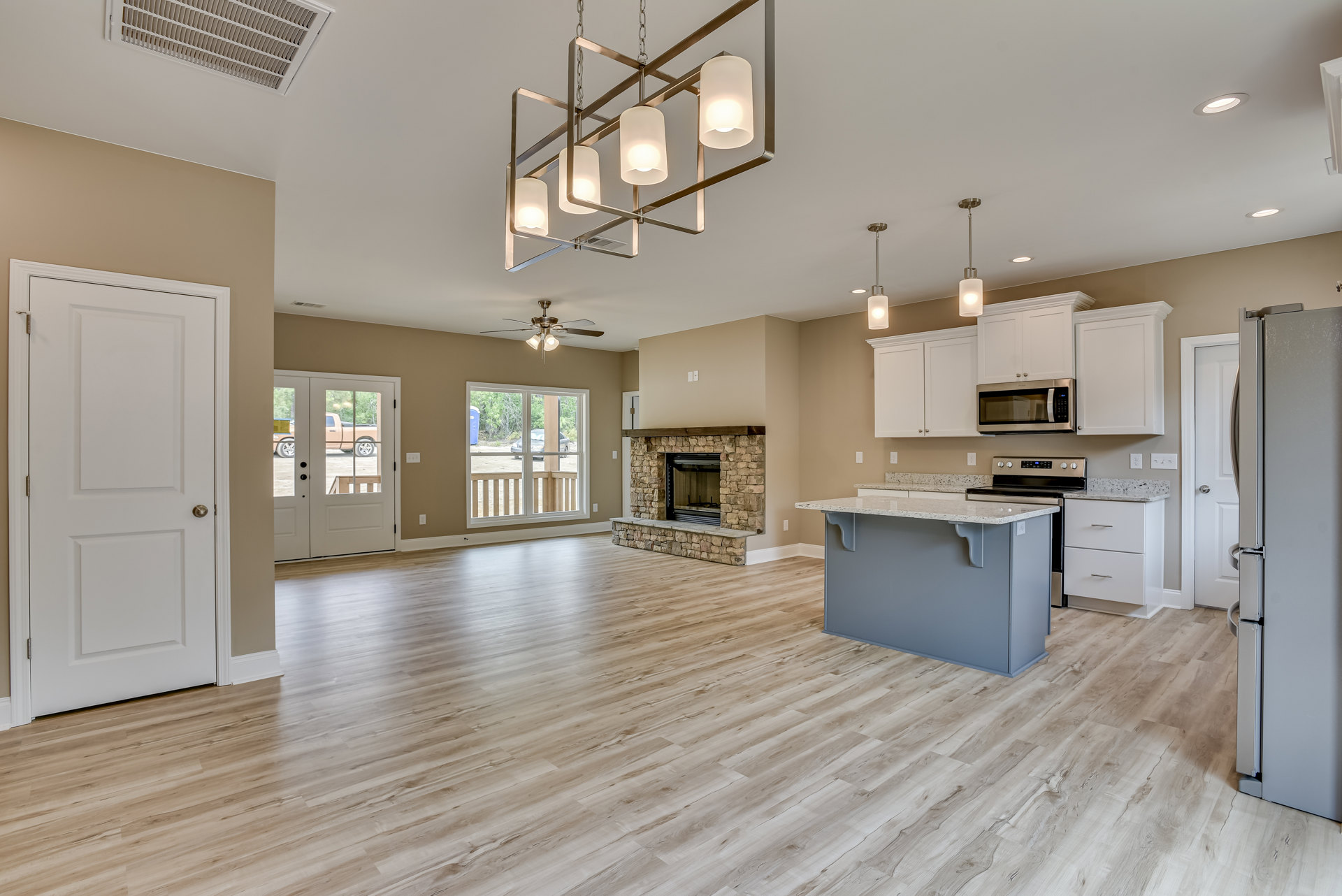 Spacious open-concept kitchen and living area featuring a central kitchen island with built-in stove, modern cabinetry, stainless steel appliances including refrigerator and