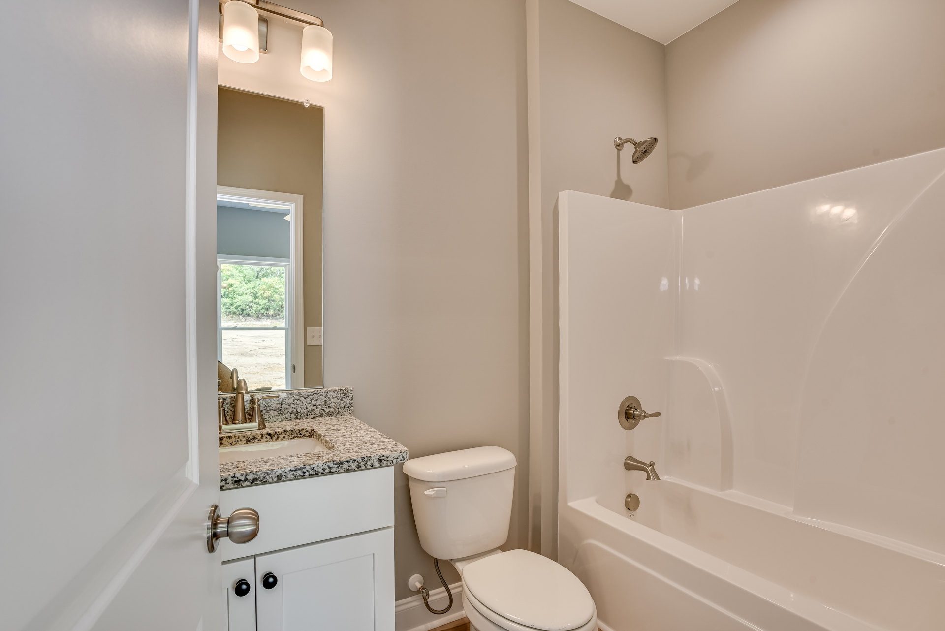 Bathroom with white tile walls, a white toilet with lid up, freestanding white bathtub, chrome faucet, and a two-bulb wall light fixture above.