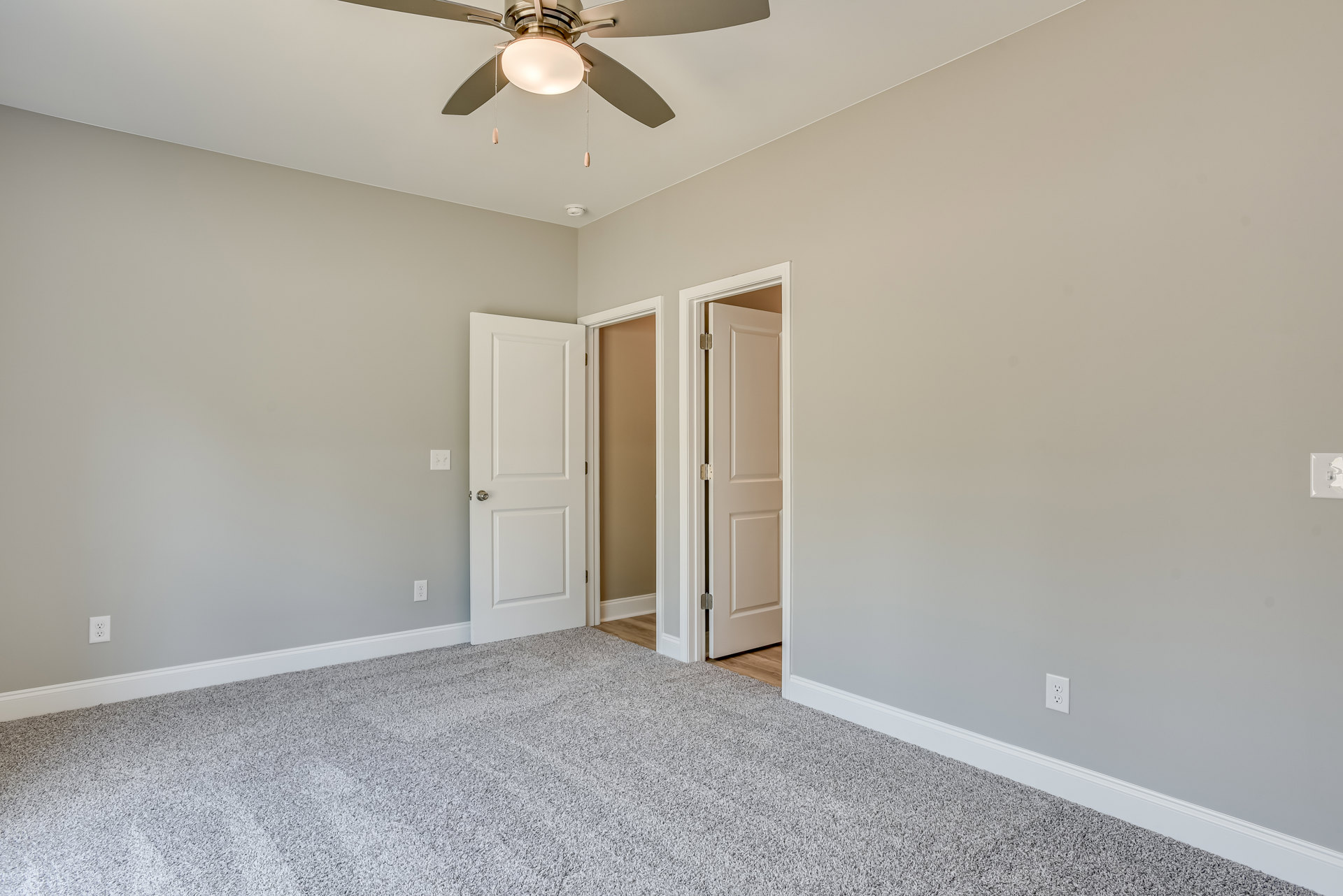 Carpeted room with white walls, ceiling fan, and two white doors featuring silver hardware
