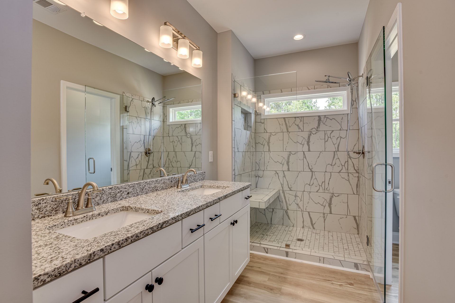 Bathroom featuring marble countertops, undermount sink, glass shower enclosure with metal handle, tile walls, and illuminated modern light fixture