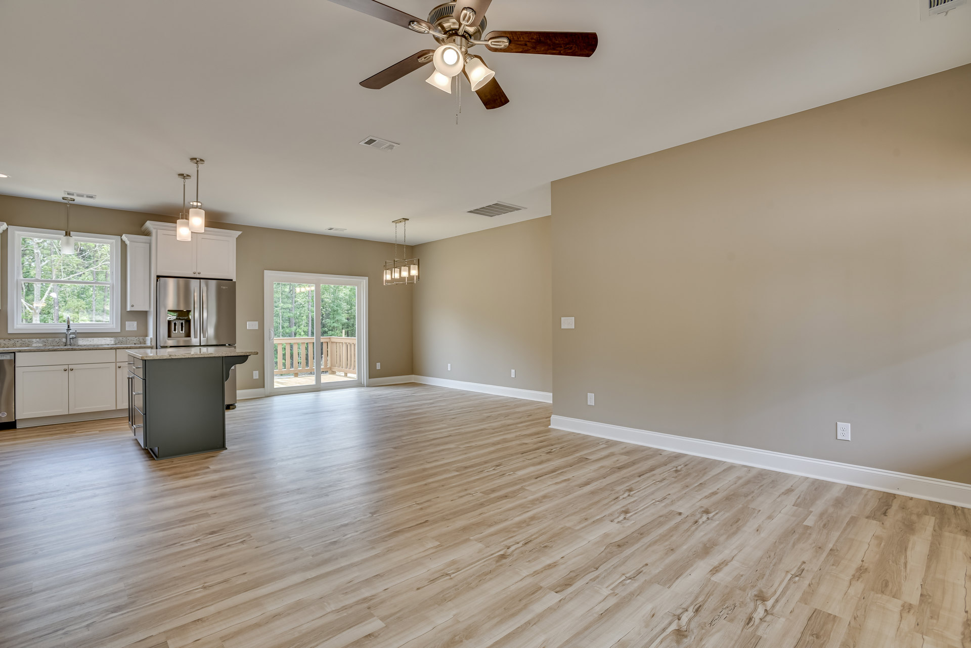 Open kitchen with marble island, ceiling fan with lights, wood flooring, sliding glass door leading to deck with trees, window above sink and modern light fixture