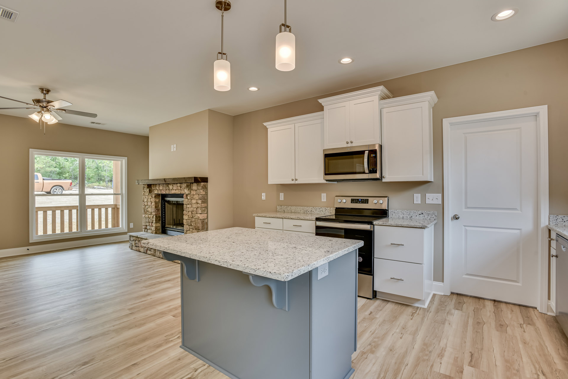 Spacious kitchen featuring a large central island with stone countertop, built-in microwave, white cabinetry, fireplace with tile surround, wood flooring, recessed lighting, and a