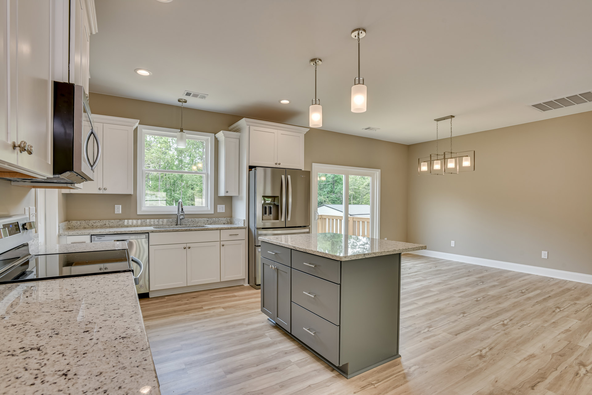 Modern kitchen featuring a marble-topped island with drawers, stainless steel refrigerator, window above a sink, and pendant light fixture.