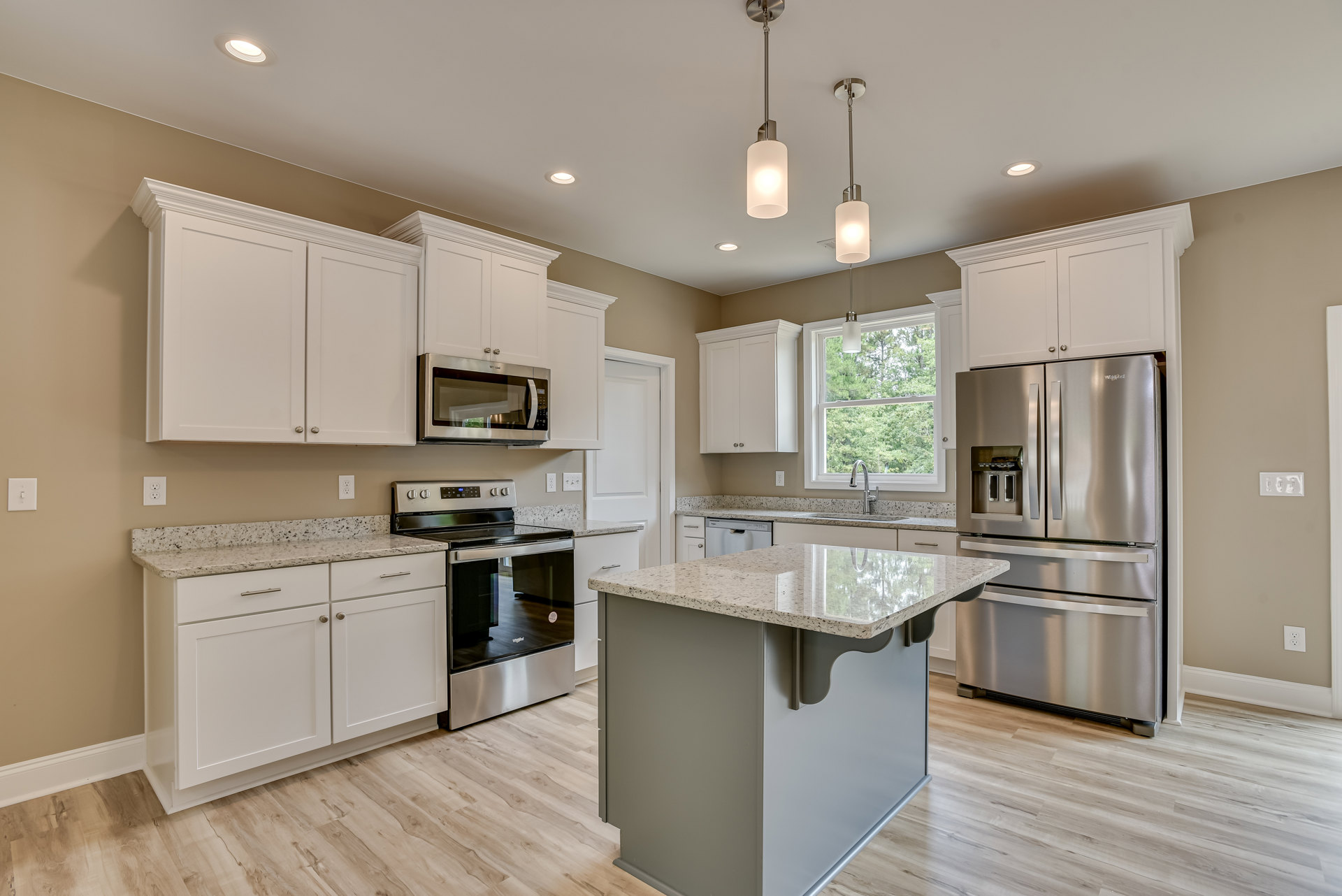 Kitchen with a granite island, stainless steel refrigerator, stove, oven, microwave with glass door, white cabinetry, and light fixtures over a polished countertop