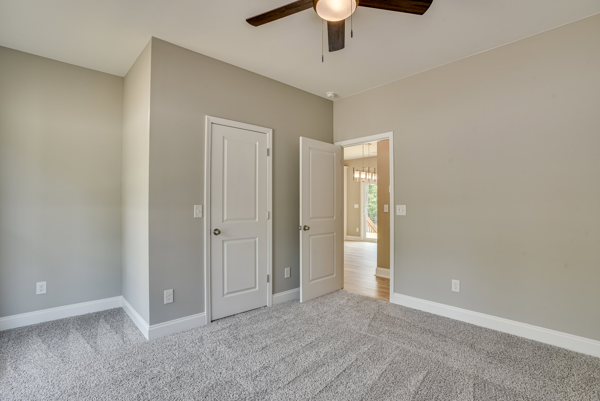 Carpeted room with two white doors, silver door knobs, ceiling fan with light fixture, white walls, and crown molding.