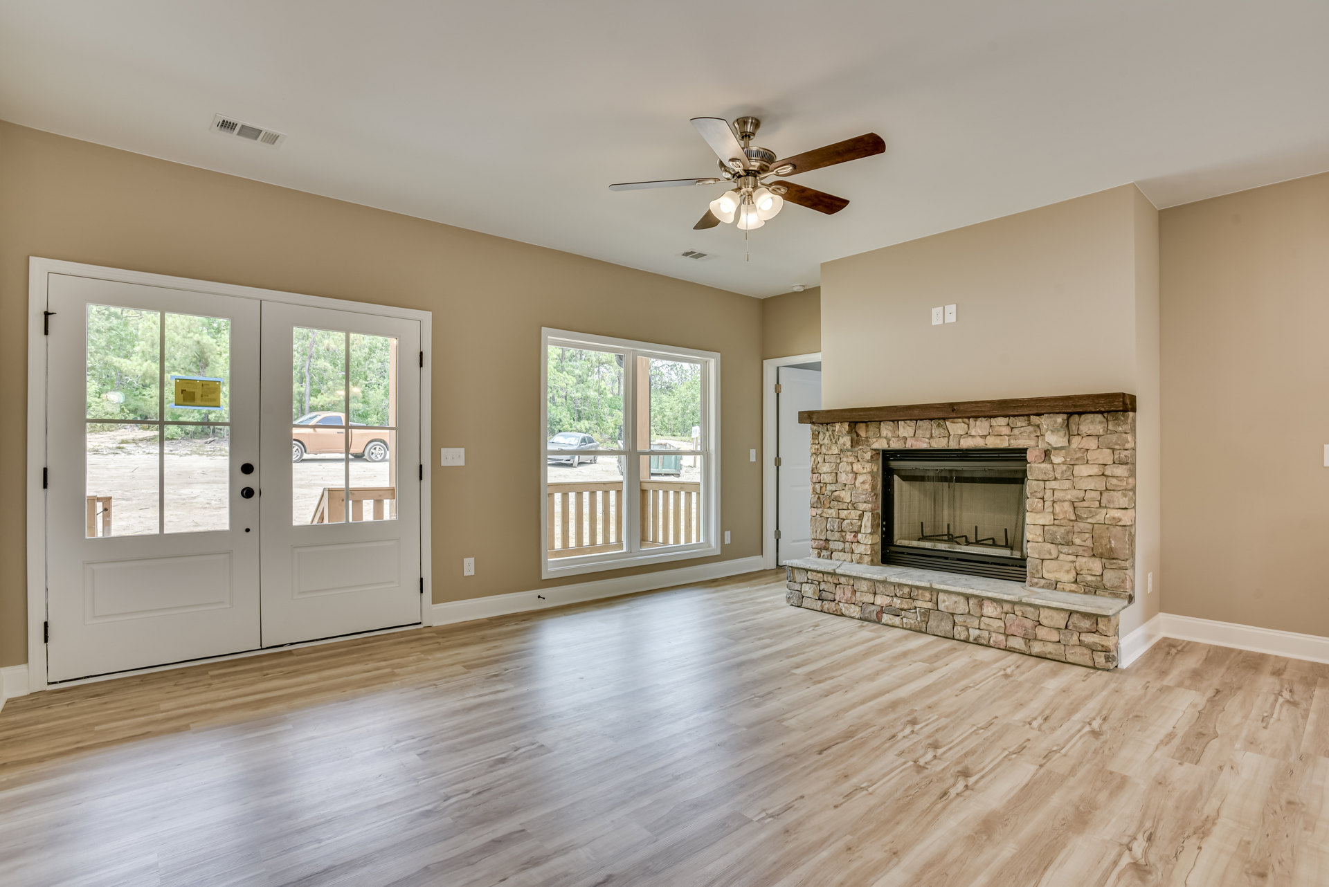 Living room with wood flooring, stone fireplace, ceiling fan with lights, double glass doors, and view of parked car outside