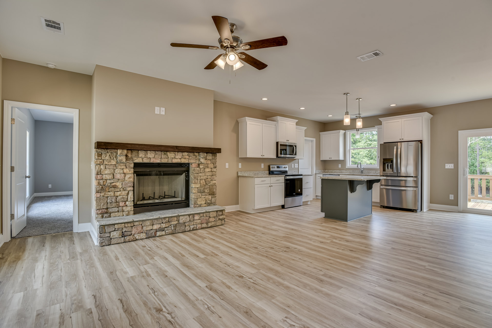 Open-concept kitchen and living room featuring wood flooring, stainless steel double-door refrigerator, built-in microwave, ceiling fan with lights, and fireplace with wire mesh