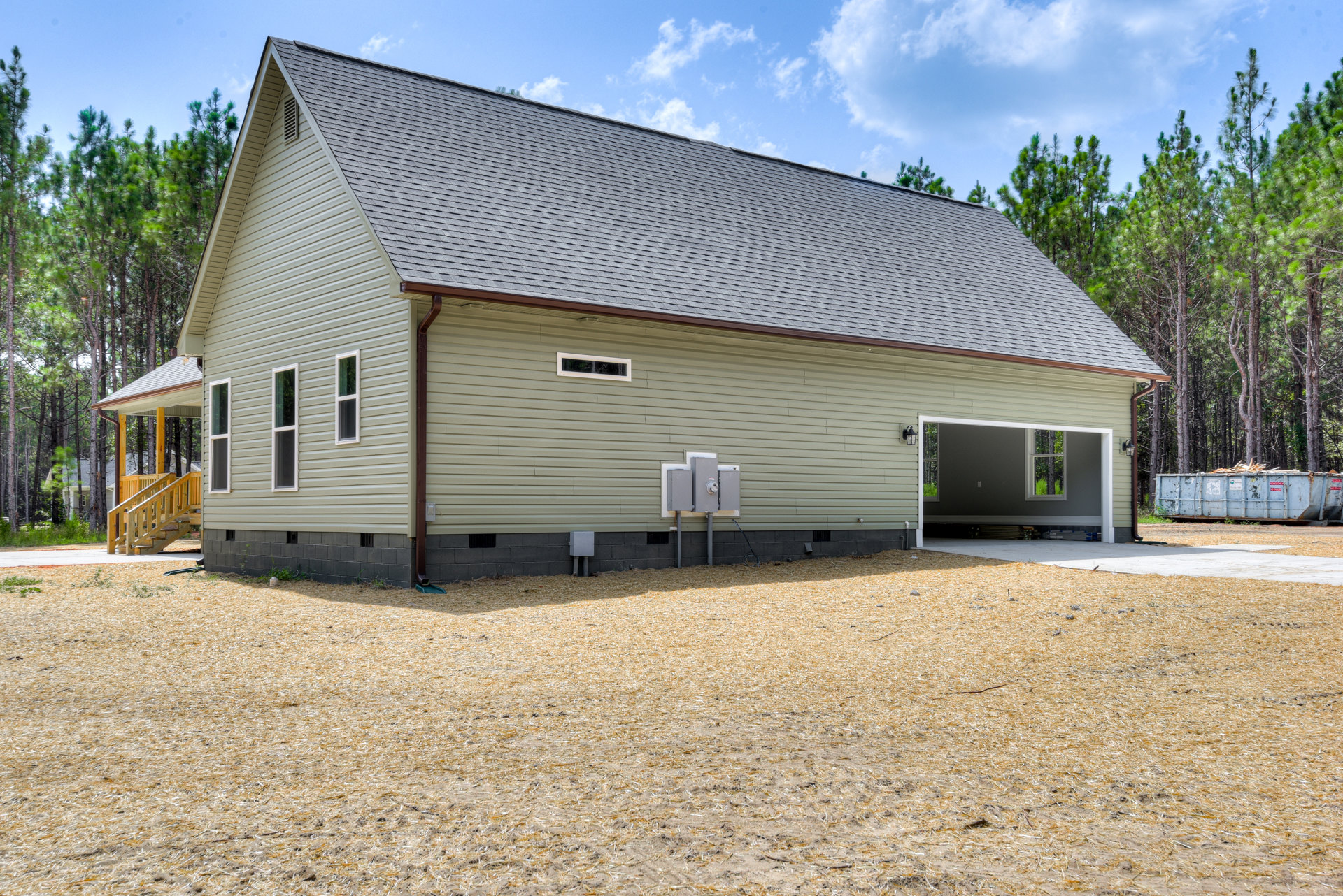 Two-story home with attached garage, gray siding, shingle roof, wooden exterior staircase, grassy front yard, and large windows.