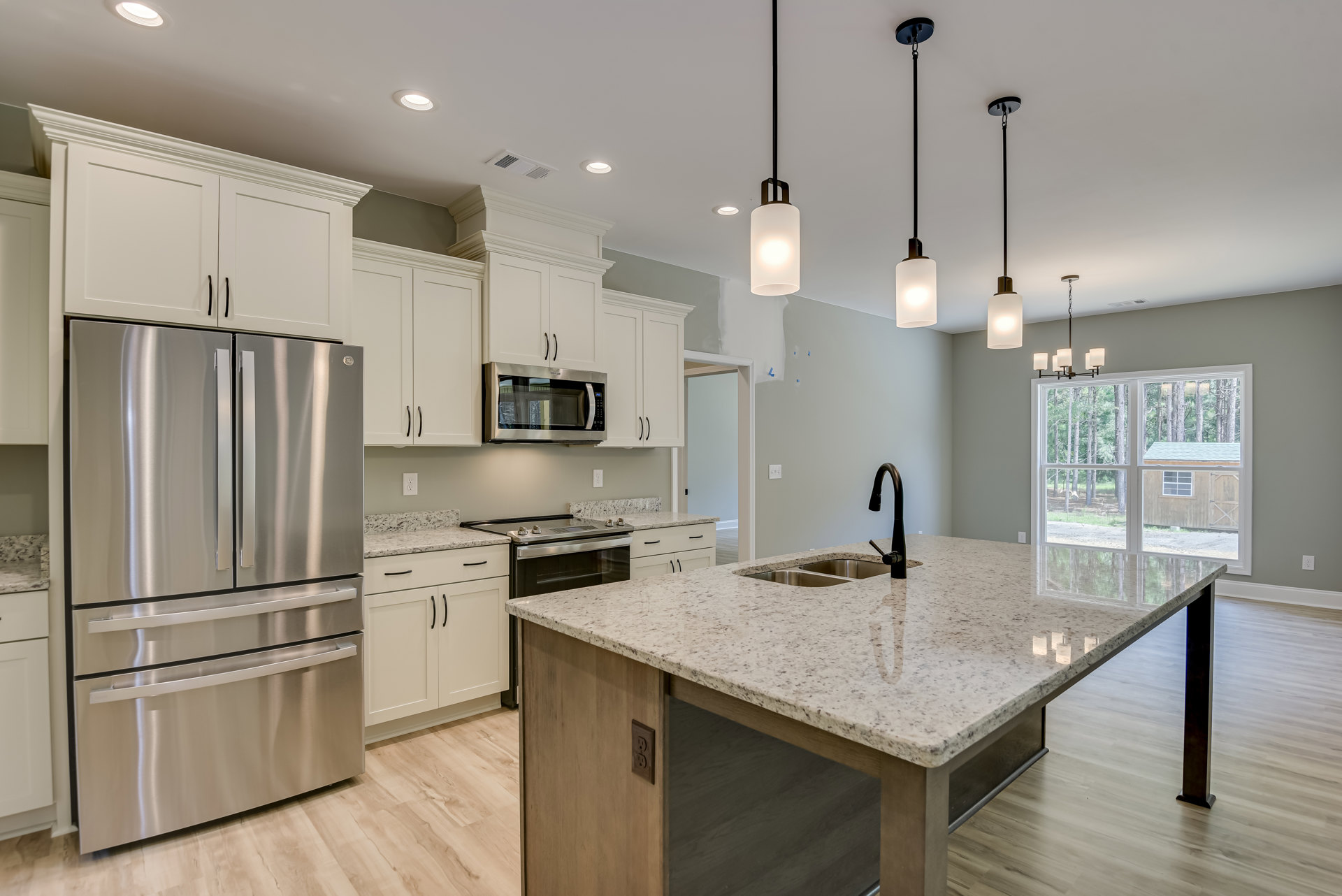 Spacious kitchen featuring a large quartz island with undermount sink and chrome faucet, stainless steel refrigerator and microwave, white tile backsplash, shaker cabinetry