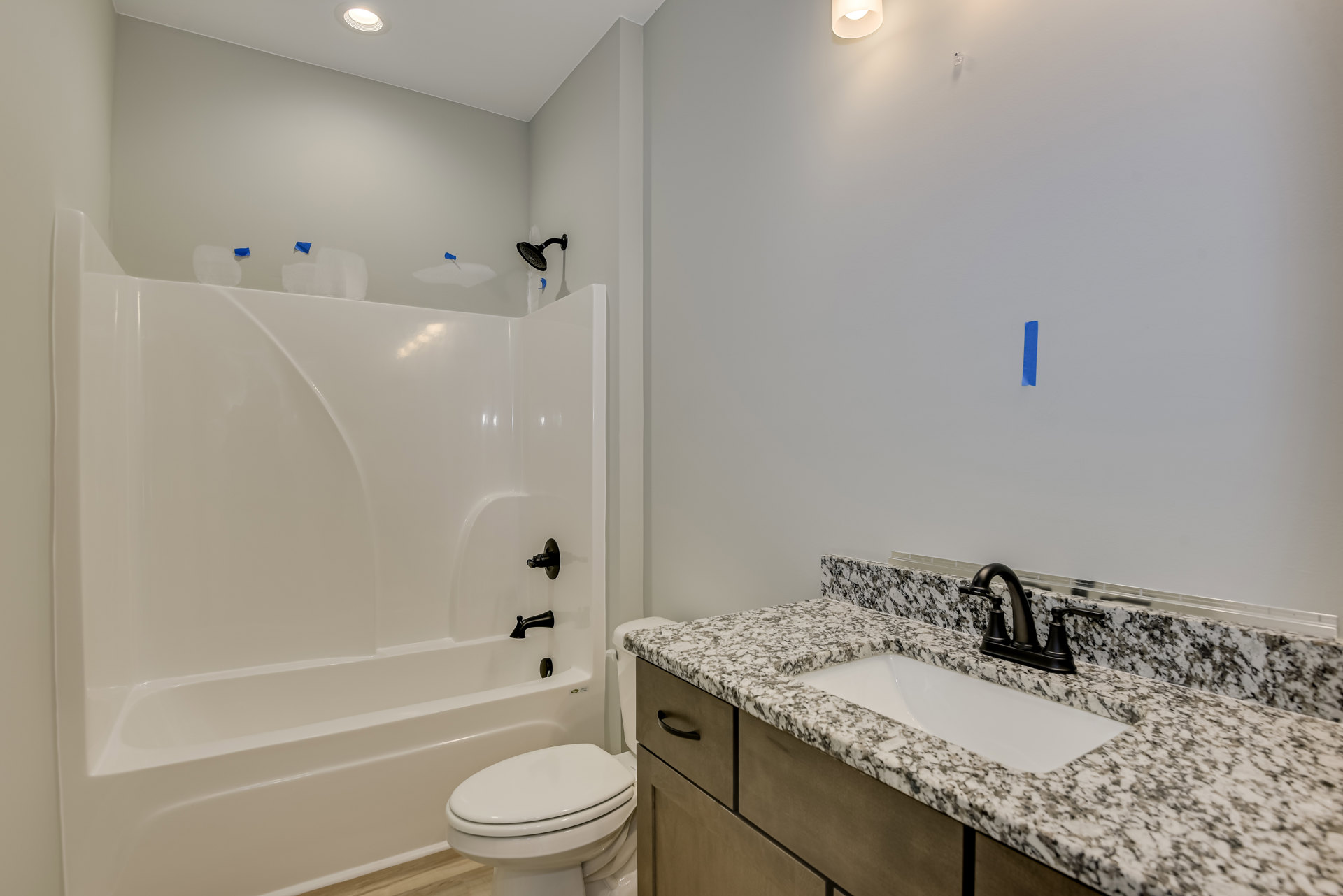 Marble countertop with black faucet, white undermount sink, white bathtub, and closed-lid toilet against light tile walls