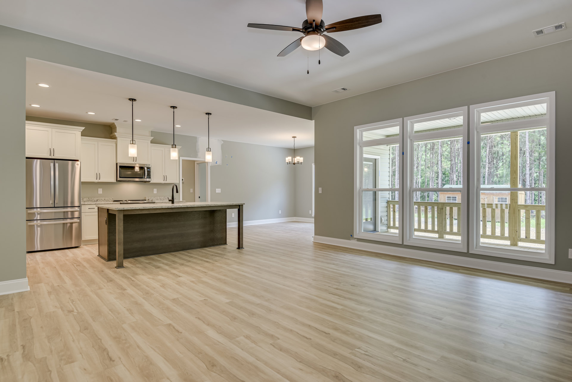 Open kitchen with wood flooring, central island featuring a sink, stainless steel double-door refrigerator, built-in microwave, cabinetry, window, and ceiling fan with light