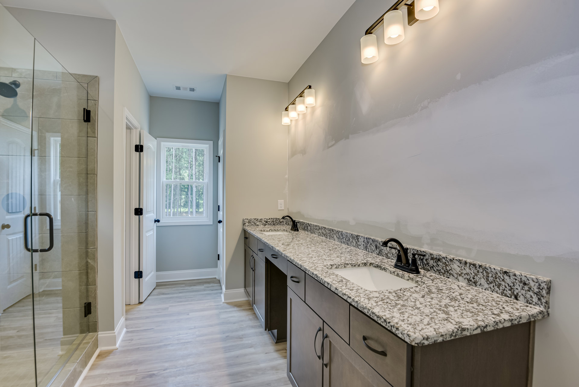 Marble countertop with white undermount sink, black and white speckled surface, chrome faucet, white cabinetry, window overlooking trees, modern light fixture with white shade