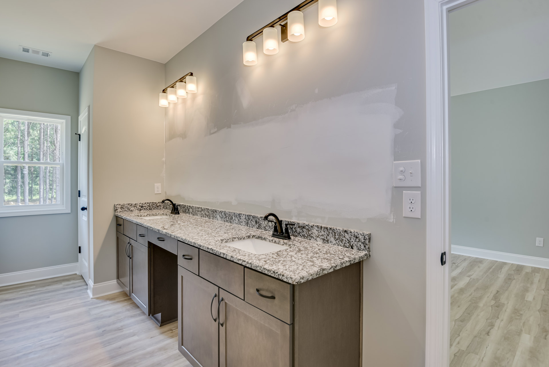 Bathroom with white tile walls, rectangular window showing green trees outside, modern wall-mounted light fixture with white shade illuminated above a sleek undermount sink set in