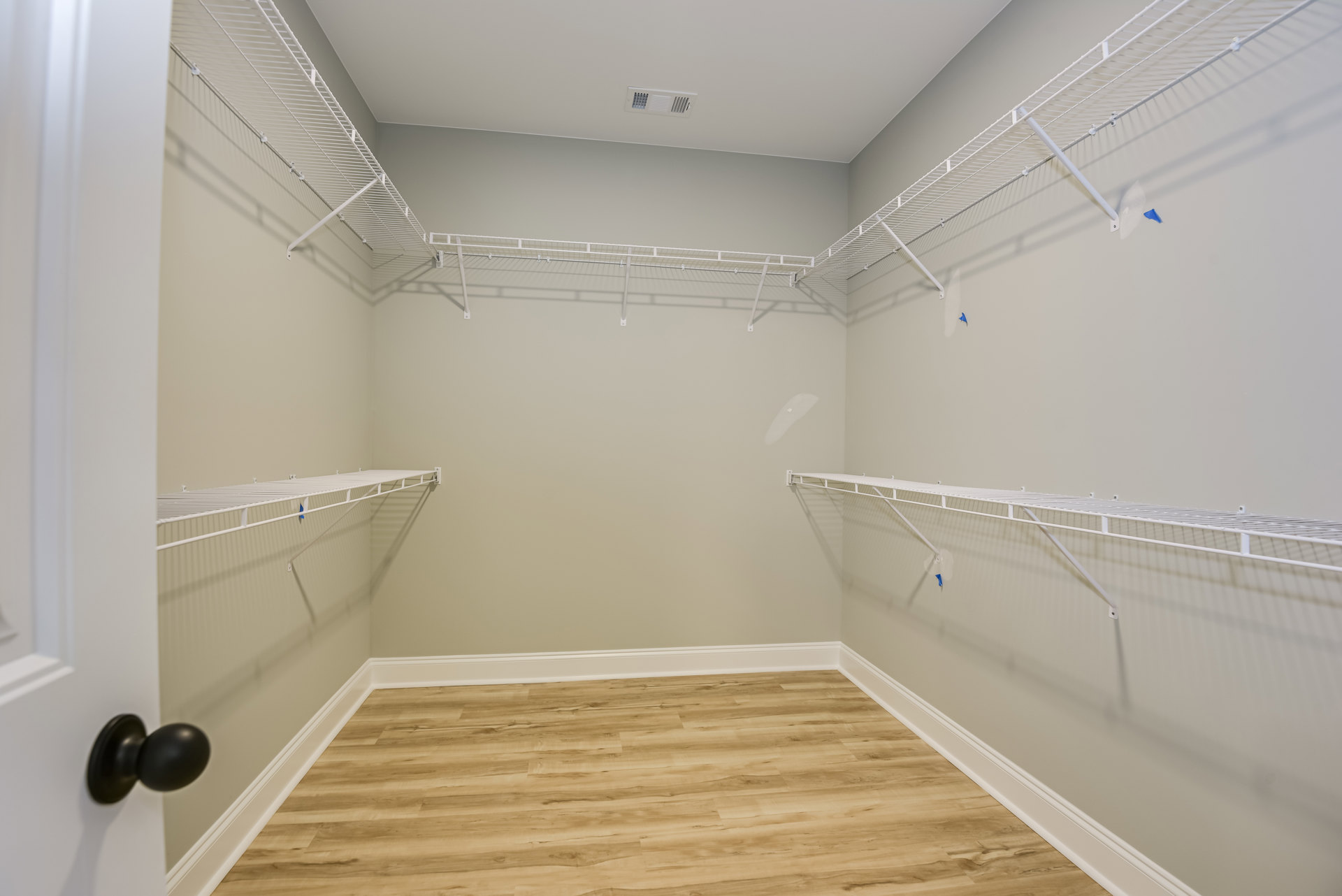 Walk-in closet with wood flooring, white baseboards, and built-in shelves; close-up of a brushed metal door knob on a white door