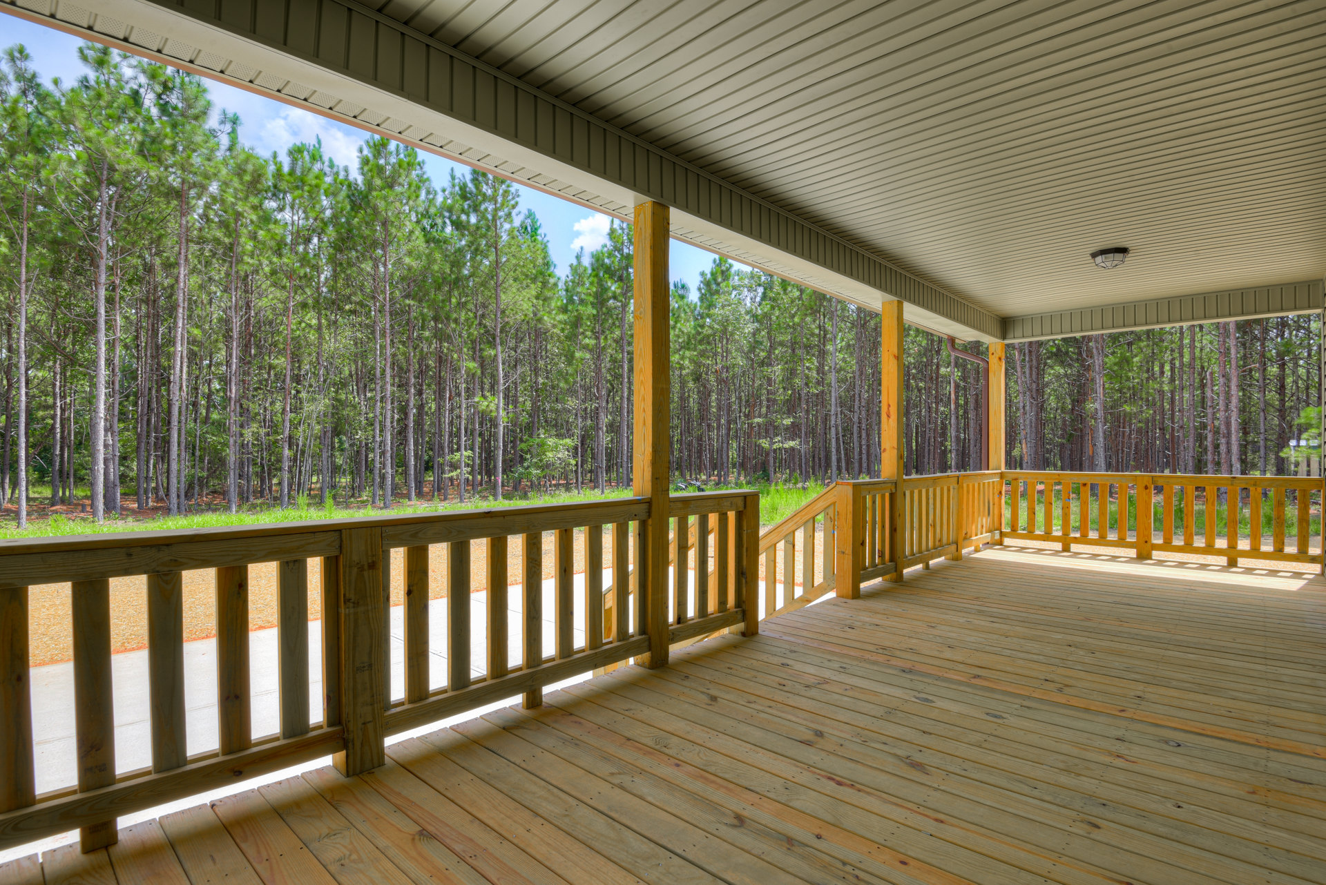 Wooden deck with railings overlooking leafy trees under a blue sky with scattered clouds