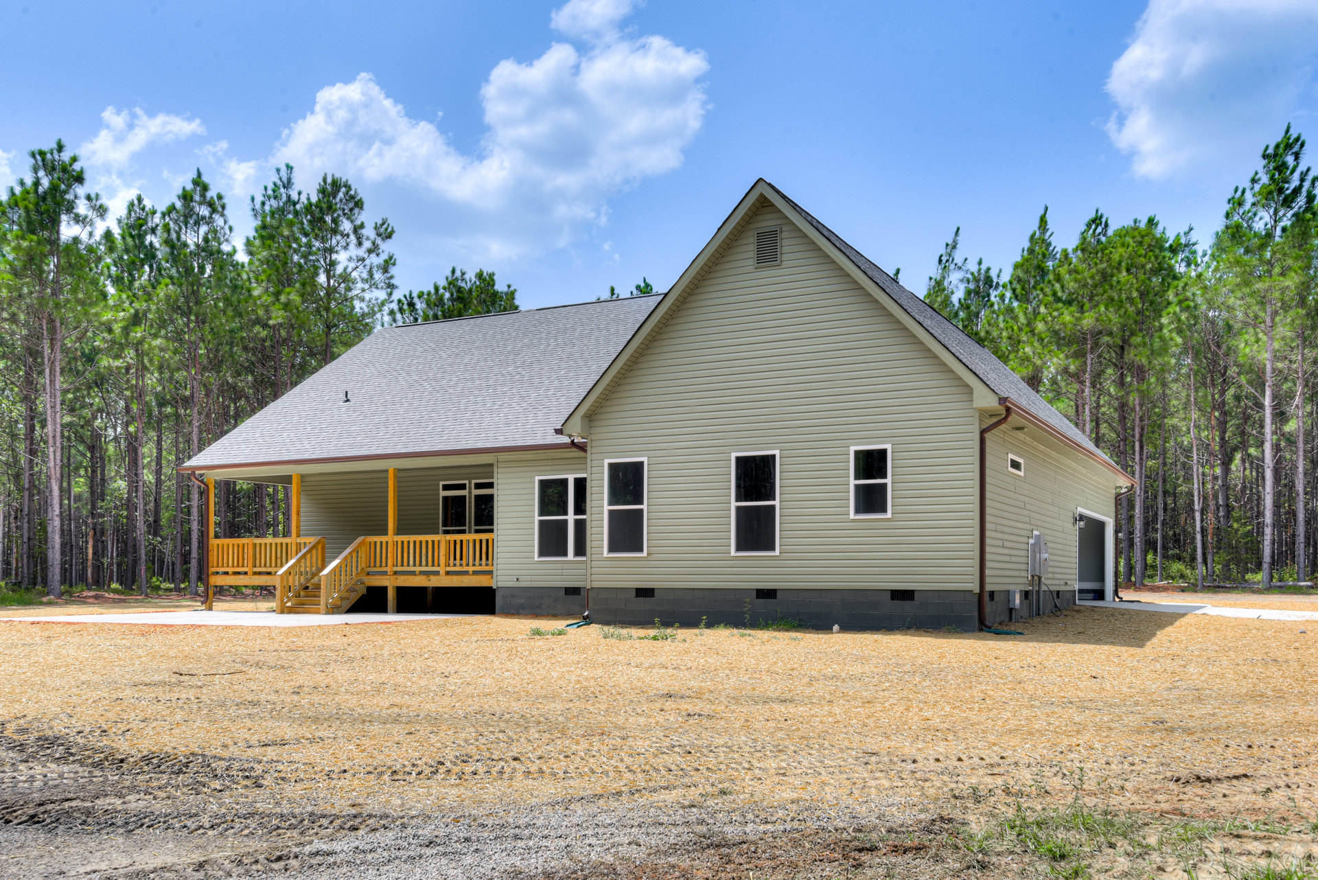 Two-story house with white-framed windows, covered front porch, paved driveway, green lawn, and mature trees under a partly cloudy sky